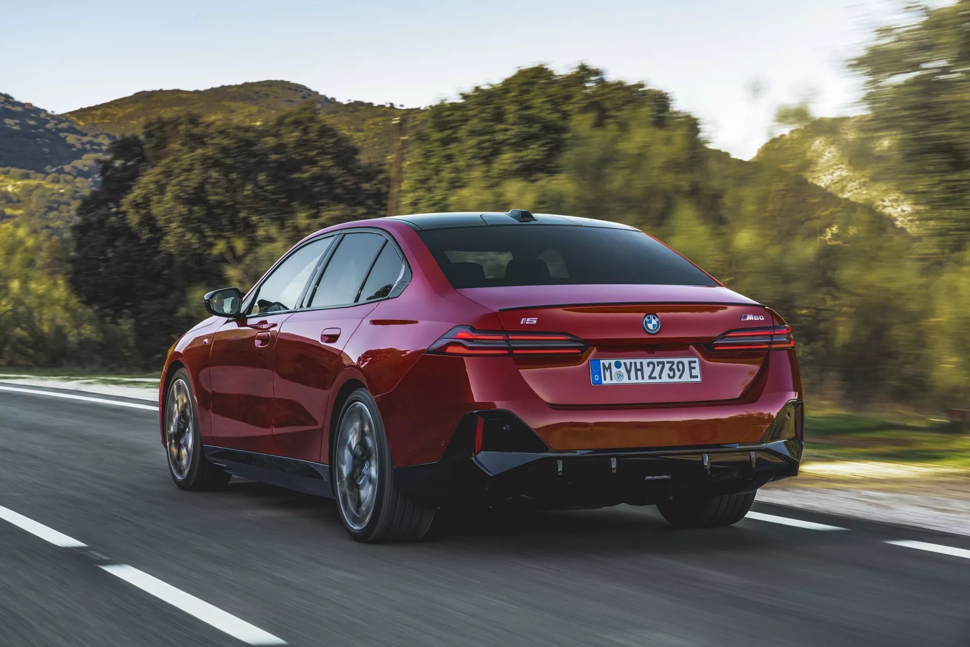 Berlina moderna BMW Serie 5 (G60-G61) del 2023 in movimento su una strada aperta, con vista posteriore da tre quarti che evidenzia i fanali posteriori eleganti, paraurti posteriore sportivo con porti di scarico integrati e una silhouette distintiva a coupé.