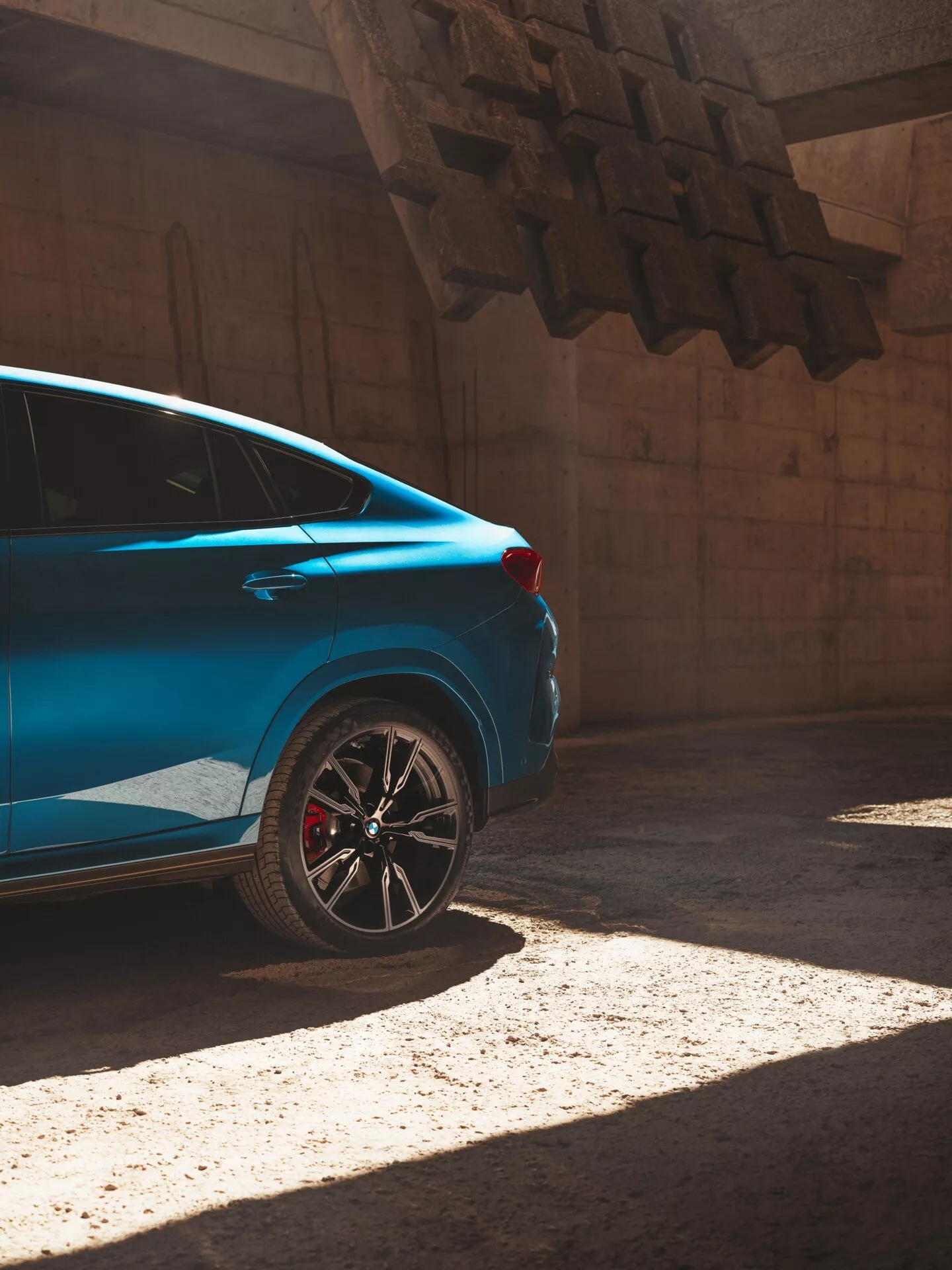 Auto blu BMW X6 2023 (G06/F96 restyling) alla luce del sole, vista da una prospettiva posteriore di tre quarti che enfatizza il quarto posteriore con cerchio sportivo e pinza freno rossa.
