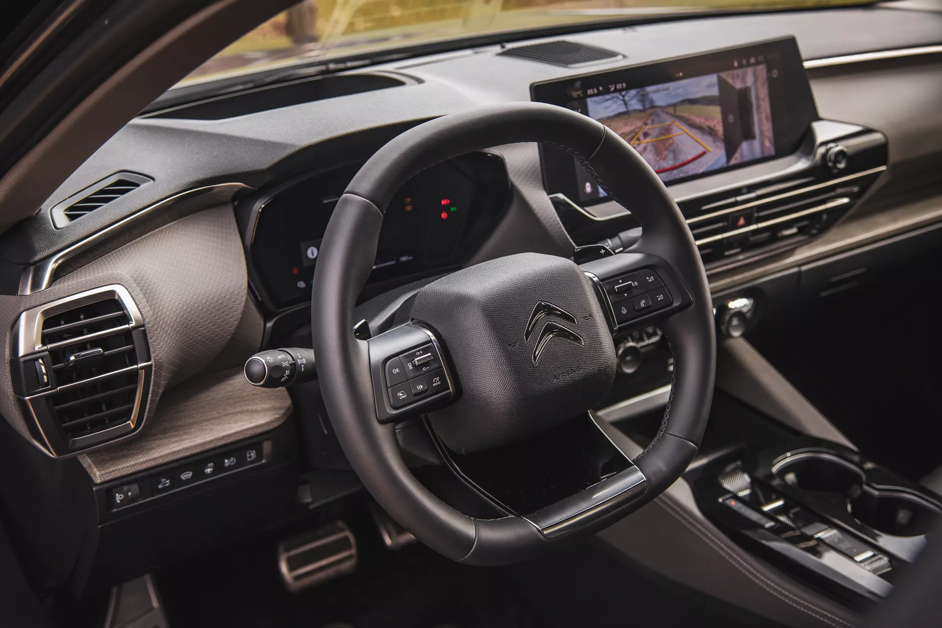 Vista ravvicinata dell'interno della Citroën C5-X 2022 che mostra il volante con pulsanti multifunzione, un display del cruscotto digitale dalla prospettiva del passeggero e un sistema di infotainment touchscreen