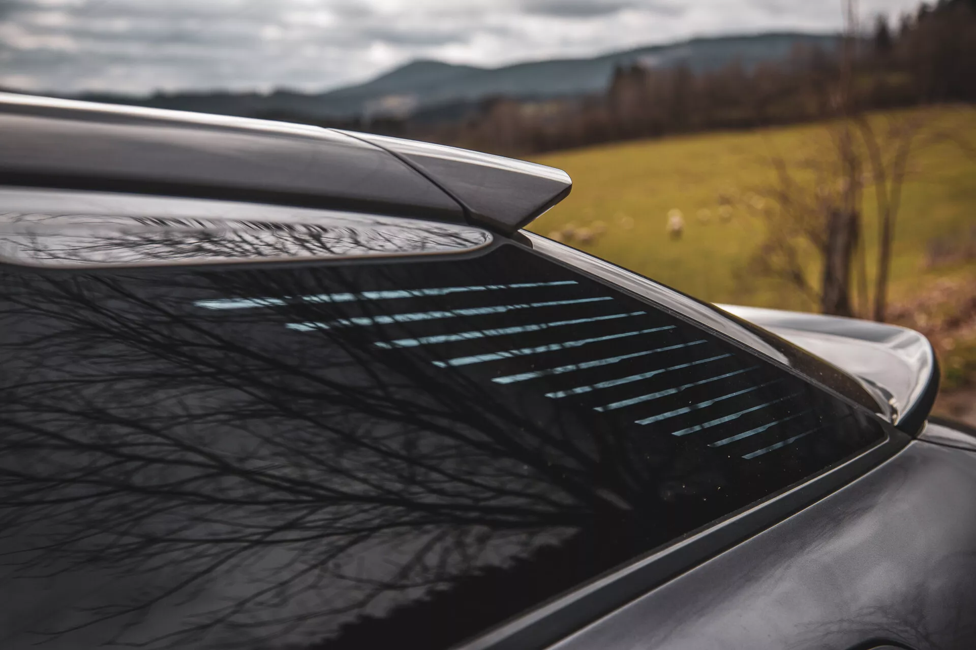Vista laterale ravvicinata della sezione posteriore della Citroen C5-X 2022 con spoiler aerodinamico integrato e lunotto termico contro uno sfondo naturale sfocato, suggerendo caratteristiche di prestazione e sicurezza del veicolo in un contesto possibilmente rurale