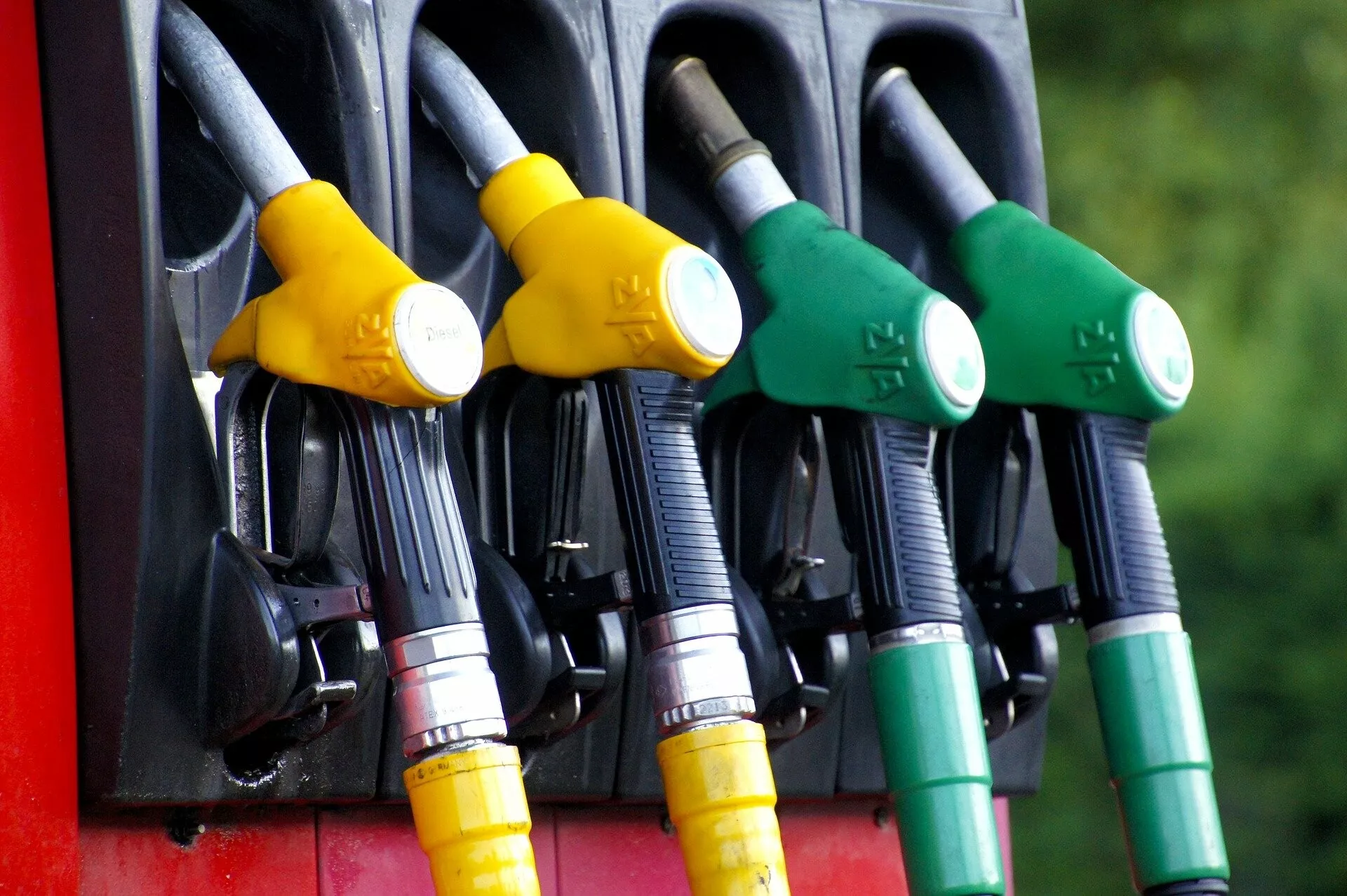 Immagine che mostra un quartetto di ugelli di pompa di carburante con maniglie colorate che indicano diversi tipi di carburante, impostati contro uno sfondo naturale delicatamente sfocato, evidenziando caratteristiche di design e sicurezza.