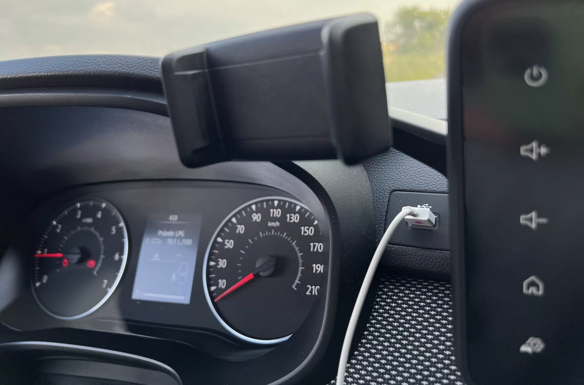 Vista dettagliata dell'interno della dashboard della Dacia Jogger 2022 che mostra il cluster strumenti, i controlli sul volante e parte del sistema di infotainment, indicando caratteristiche come il tachimetro analogico, il contagiri, display digitale per 'Nessun Audio' e capacità di ricarica dello smartphone.