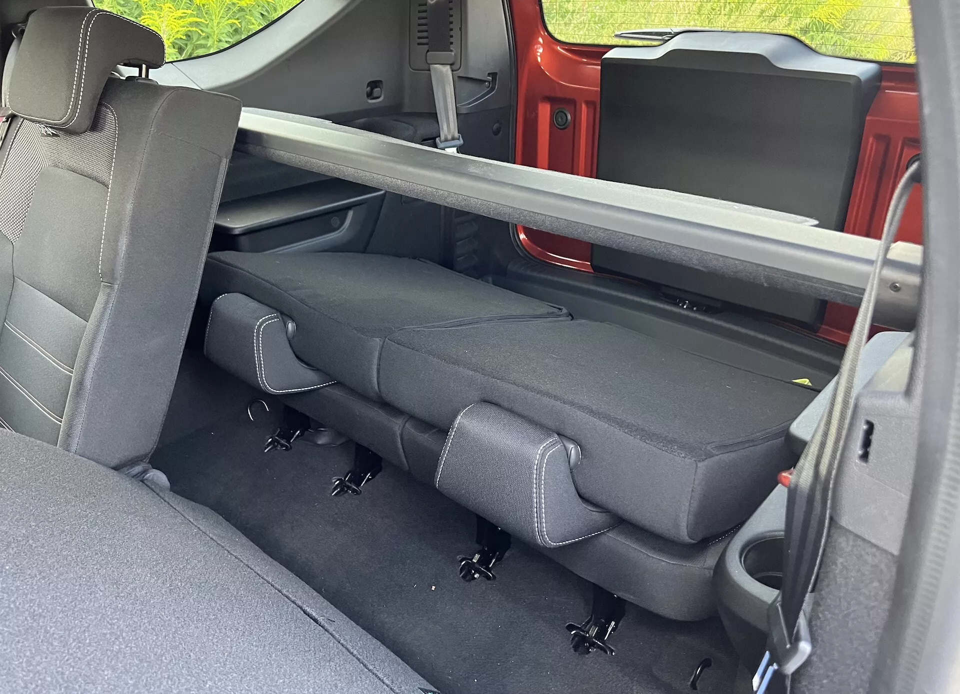 Vista interna della Dacia Jogger 2022 incentrata sul comparto passeggeri posteriore con tappezzeria scura, cinture di sicurezza retrattili, sistema LATCH e meccanismo di sedili pieghevoli visto dalla porta posteriore lato passeggero.