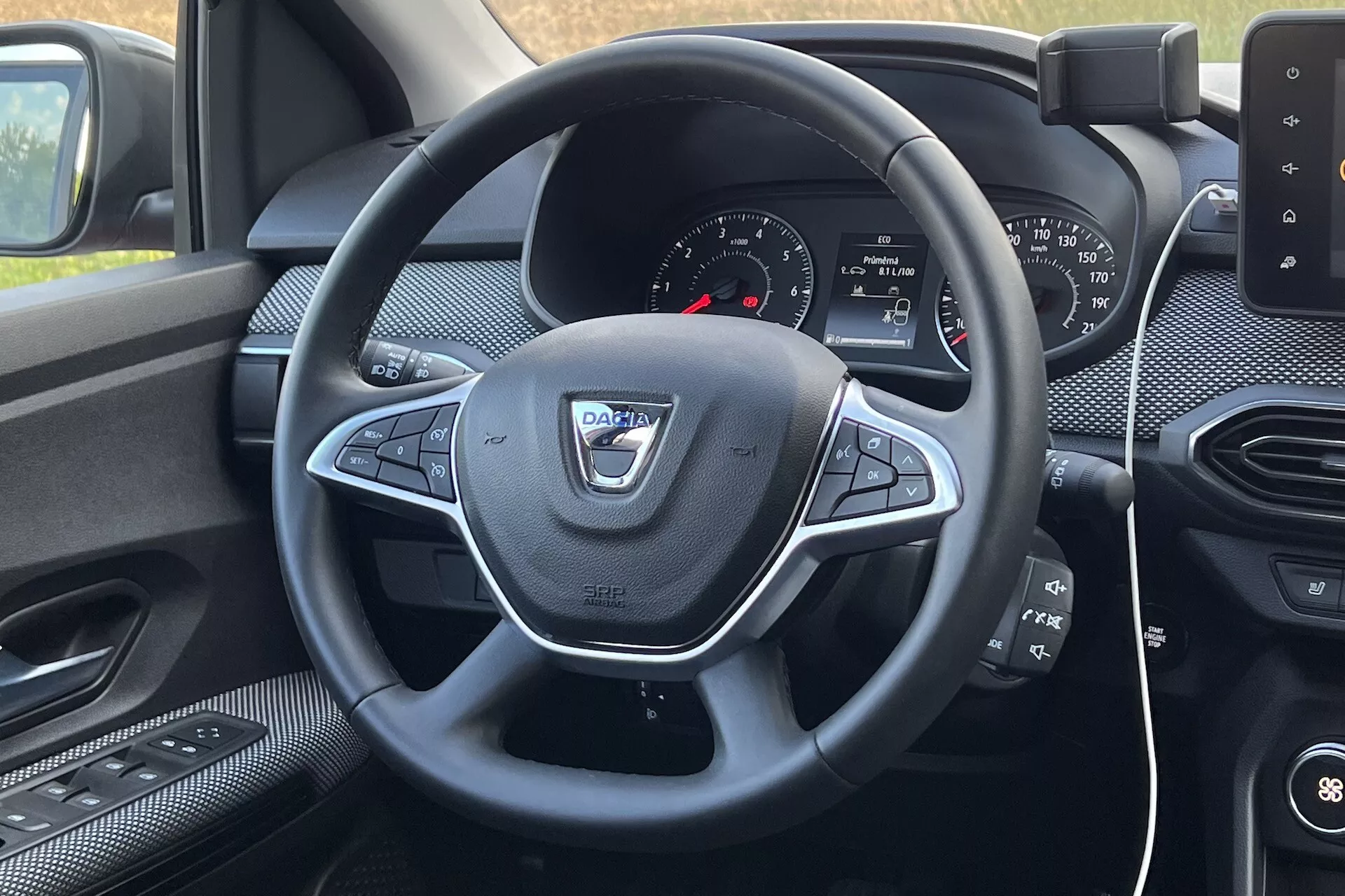 Vista interna del Dacia Jogger 2022 dal sedile del guidatore, focalizzata sul volante con comandi multifunzione e cruscotto con sistema infotainment
