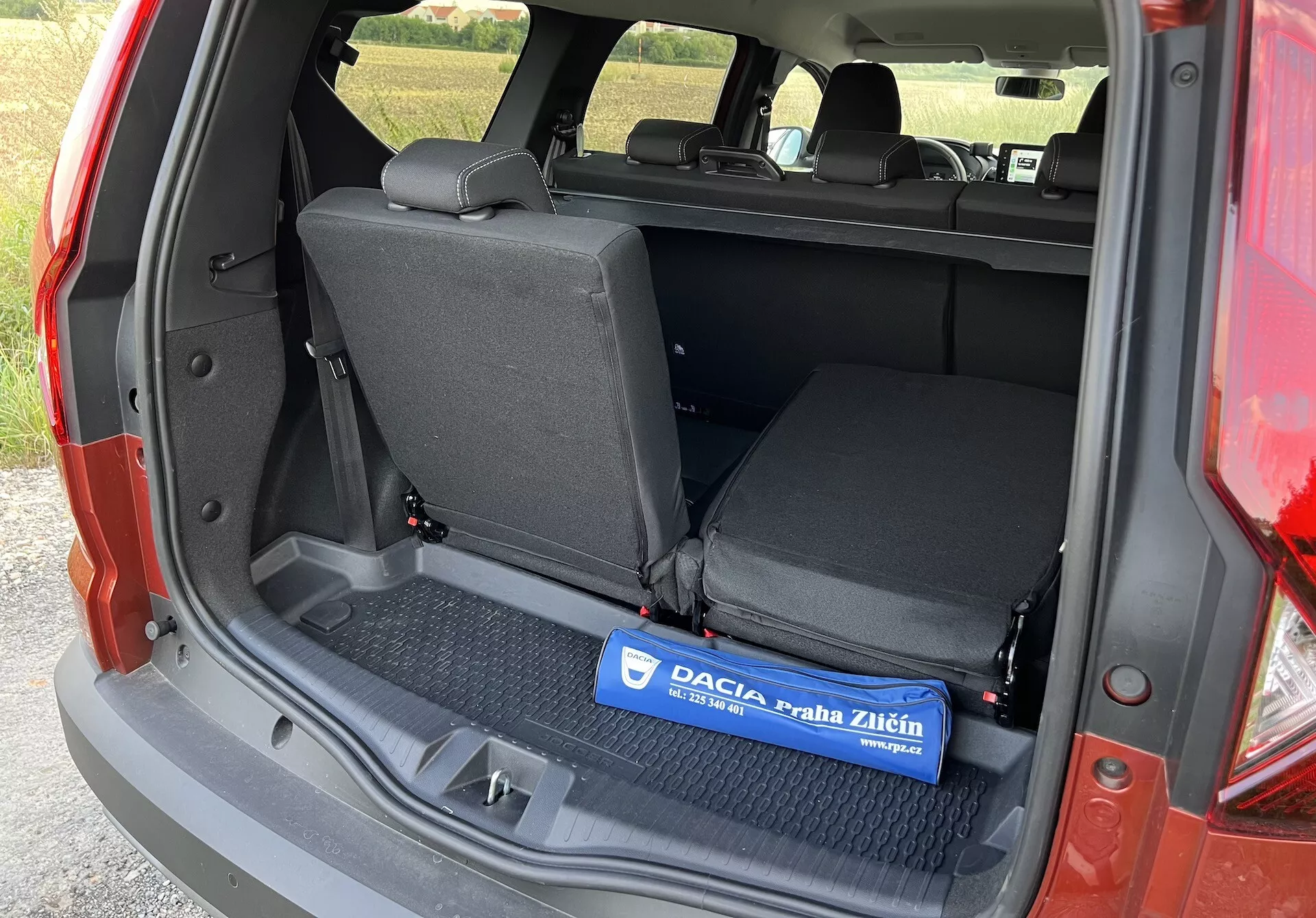 Dacia Jogger 2022 mostrando spazio di carico interiore da un angolo laterale sinistro con portellone aperto, presentando una zona di carico piatta con tappetino in gomma, sedili posteriori ribaltabili 60/40 e dettagli dei rivestimenti laterali senza componenti di tecnologia avanzata o lusso visibili
