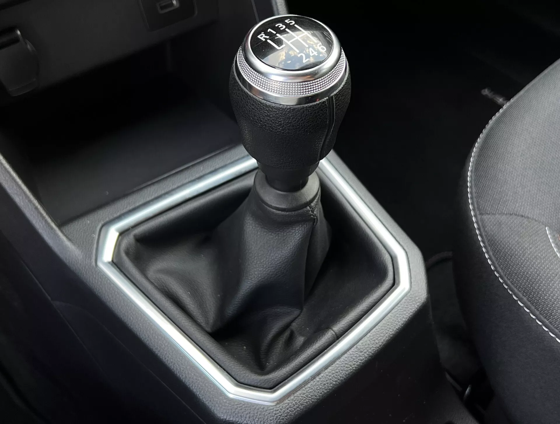 Vista ravvicinata della leva del cambio manuale Dacia Jogger 2022, mostrando un schema di cambiata a 6 velocità, leva coperta in pelle e inserto esagonale metallico in un interno di auto raffinato