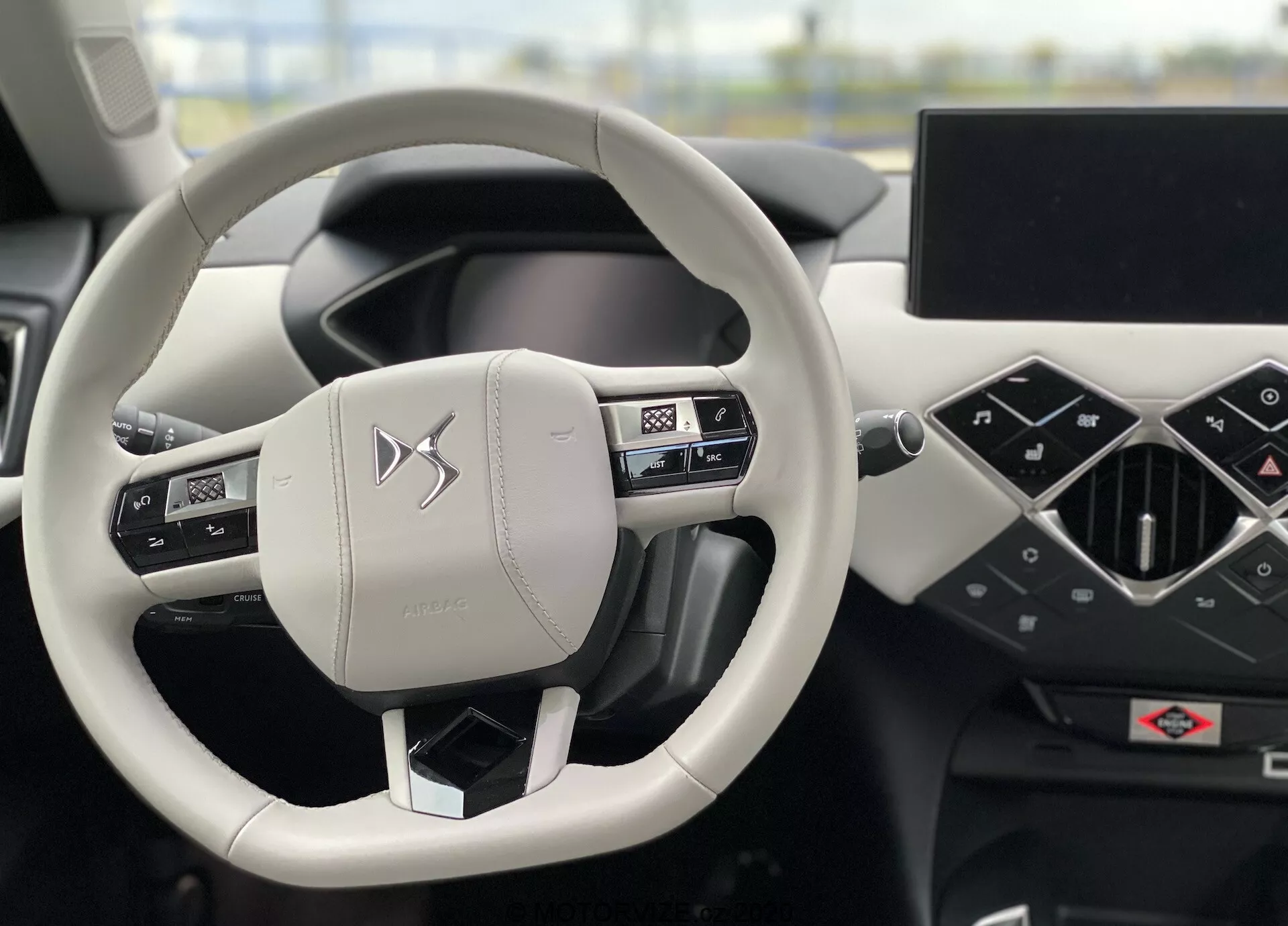 Vista interna della DS Automobiles DS-3 Crossback E-Tense 2019 con focus sul volante e il cruscotto dalla prospettiva del conducente. Il volante a due razze, rivestito in pelle con cuciture, include comandi integrati per audio, telefono e impostazioni del veicolo. Il cruscotto presenta un quadro strumenti digitale e un ampio touch screen infotainment orientato orizzontalmente. Il design minimalista e moderno e i materiali pregiati enfatizzano un'esperienza di veicolo premium.
