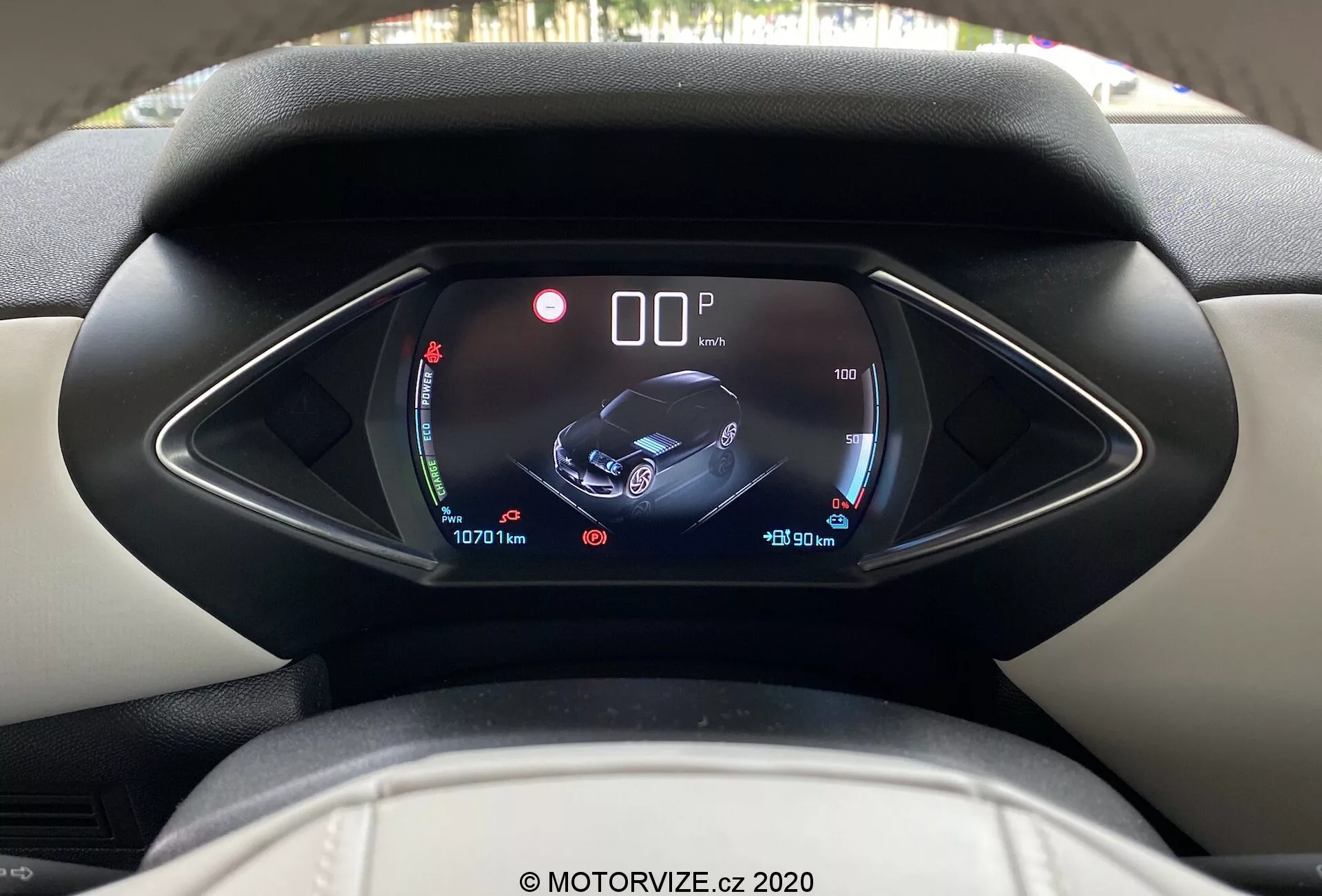 Vista interna del DS Automobiles DS-3 Crossback E-Tense 2019 dalla prospettiva del conducente, con particolare attenzione al quadro strumenti digitale con un'unica cappottina asimmetrica. Il display mostra indicatori di batteria e temperatura, un grafico centrale dell'auto con icone di sicurezza e assistenza, e informazioni sui dati del viaggio e letture del contachilometri, indicando caratteristiche interne moderne e ad alta tecnologia. Immagine chiara e a fuoco, filigrana MOTORVIZE.cz 2020.