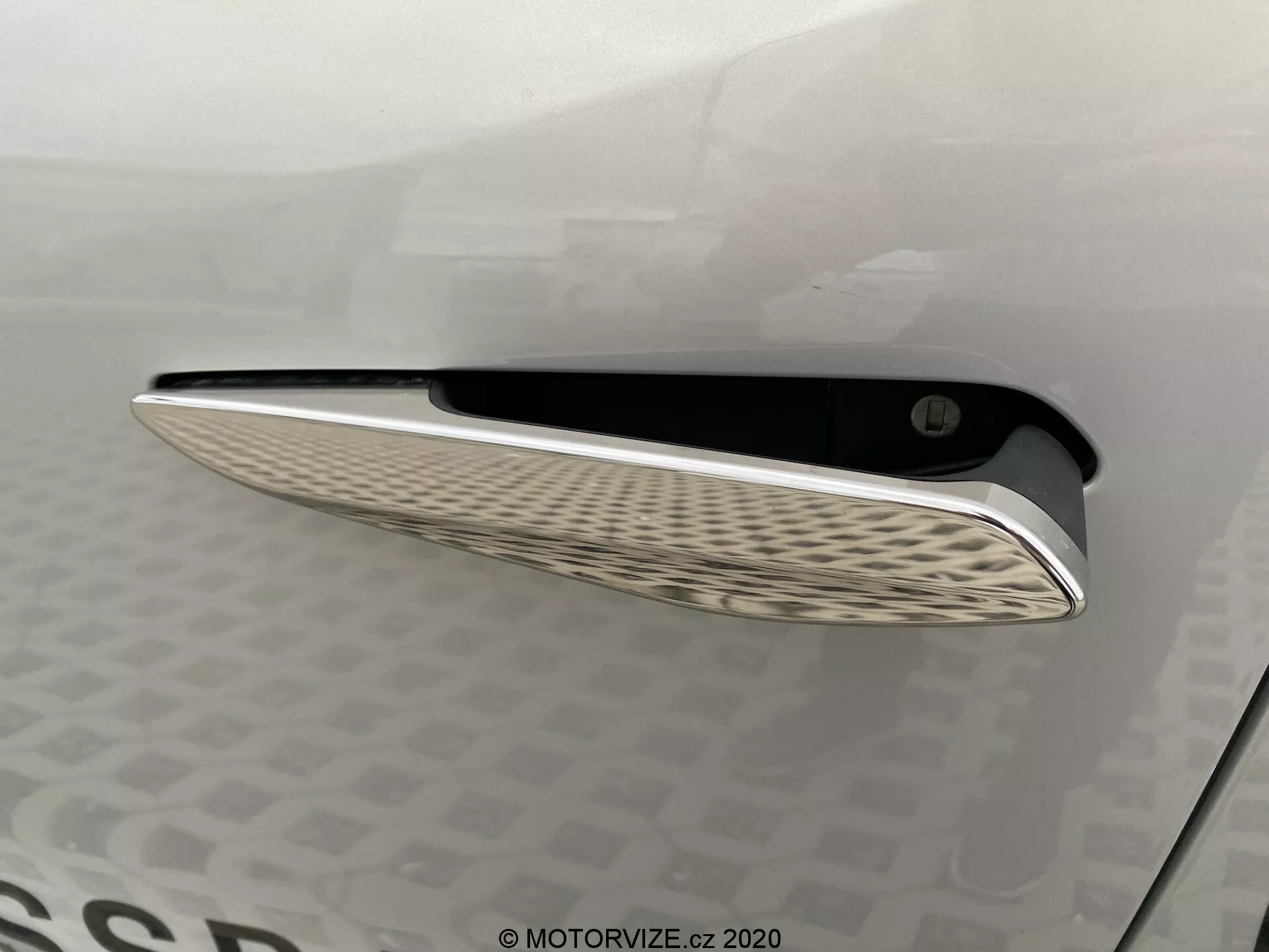 Vista ravvicinata della bocchetta della DS Automobiles DS-3 2019 (DS-3 Crossback E-Tense), caratterizzata da una rifinitura cromata elegante e da un distintivo motivo ondulato nella griglia interna, catturata da un angolo laterale con illuminazione soffusa per evidenziare la curvatura e gli elementi di design del pannello della carrozzeria.