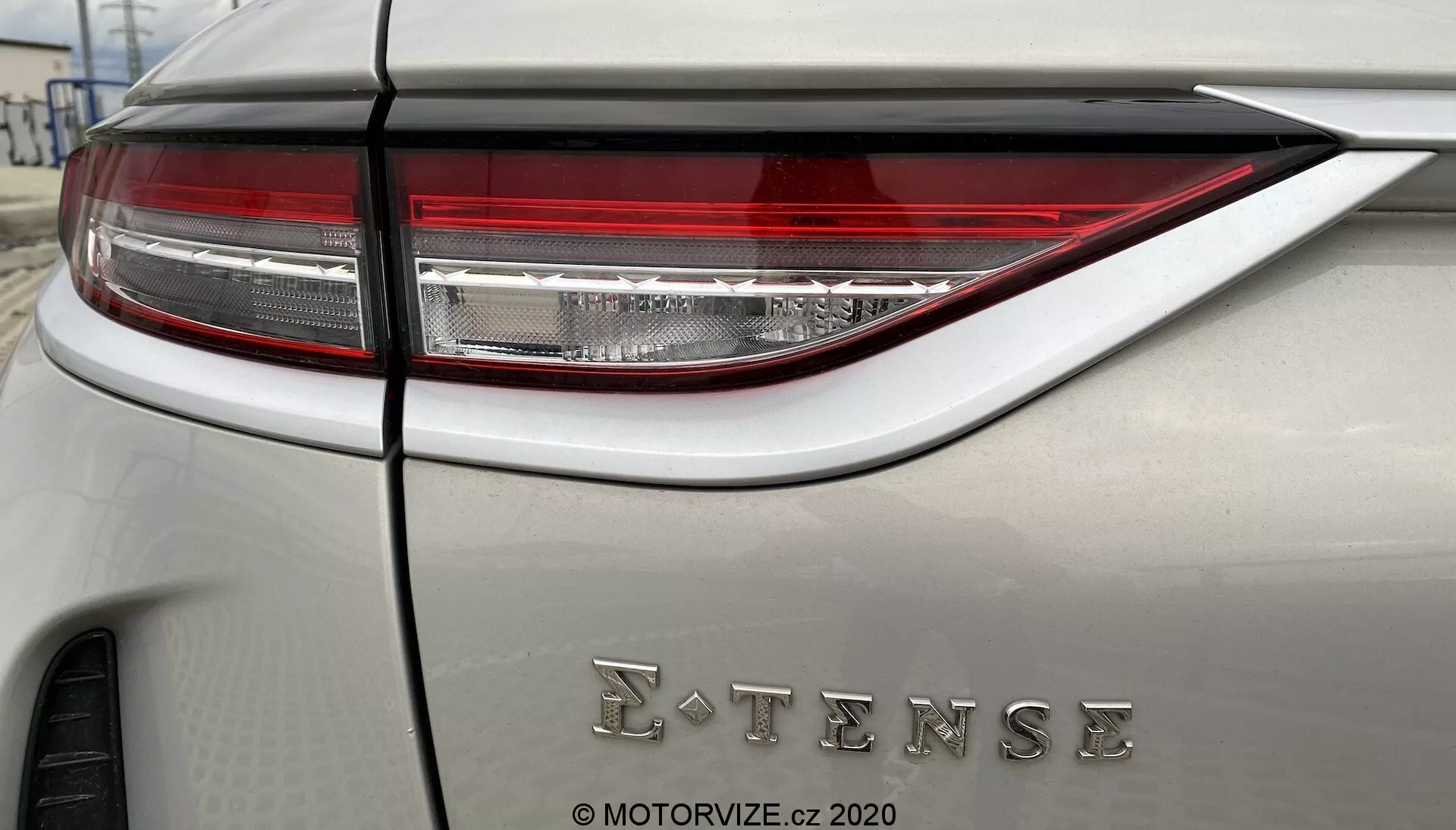 Primo piano dettagliato del pannello posteriore del DS Automobiles DS-3 2019 (DS-3 Crossback E-Tense) che mostra il sofisticato gruppo ottico posteriore a LED e il badge E-TENSE, che indica tecnologia elettrica o ibrida. La carrozzeria dell'auto è di un colore neutro con finitura opaca o satinata.