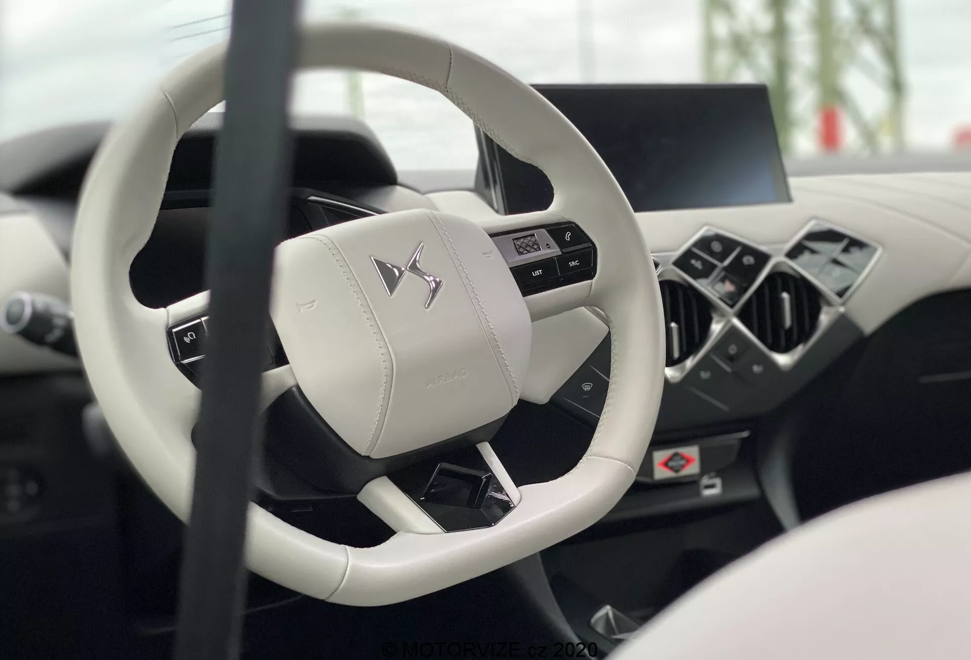 Interni di DS Automobiles DS-3 2019 (DS-3-Crossback-E-Tense) dal sedile del conducente, con messa a fuoco sul volante moderno a tre razze con fondo piatto e pulsanti multifunzionali e cruscotto digitale sfocato e console centrale che mostrano lusso e tecnologia avanzata