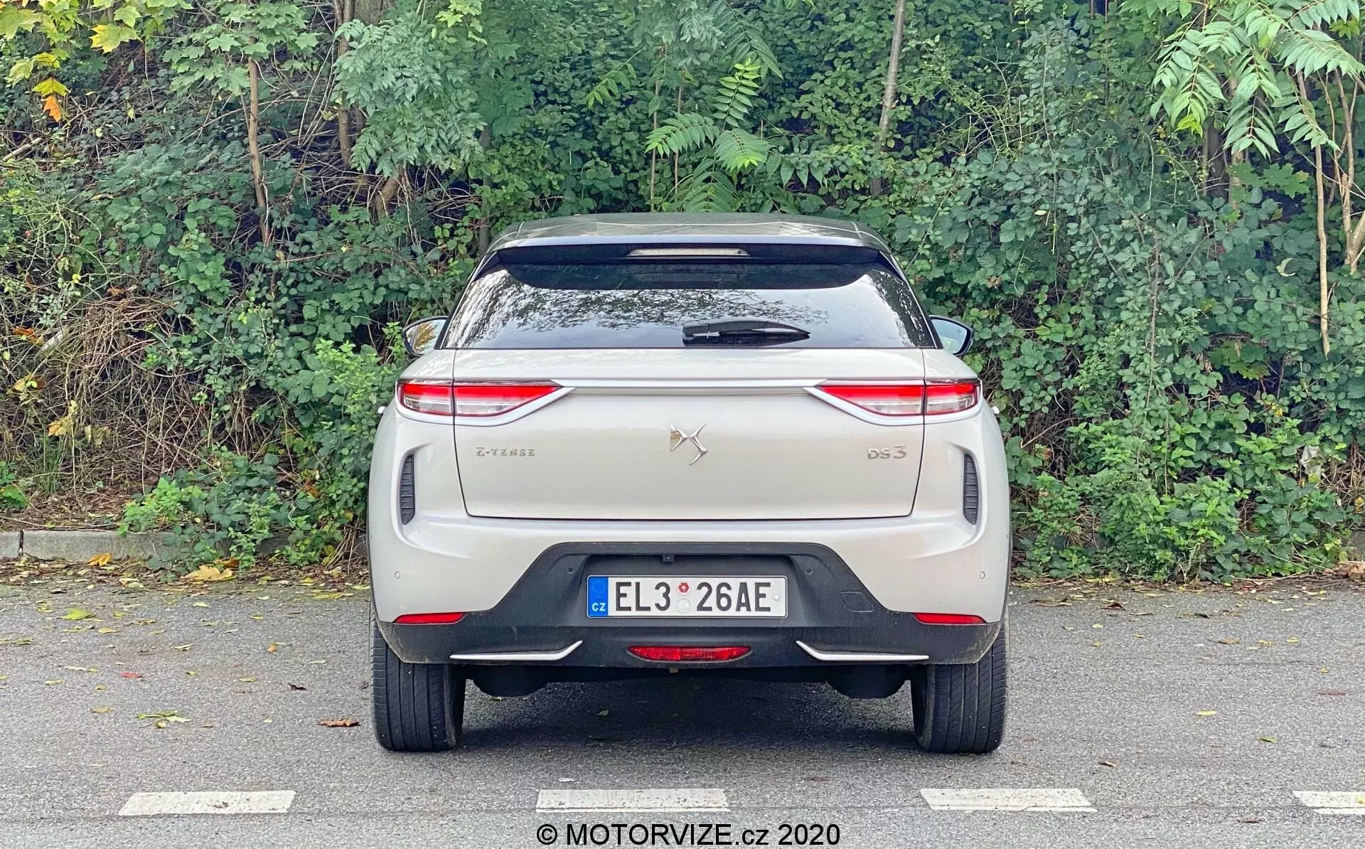 L'immagine mostra una vista posteriore della DS Automobiles DS 3 Crossback E-Tense 2019, fotografata a livello degli occhi e focalizzata sulla parte posteriore. Le caratteristiche visibili includono una targa centrata, distintivi del marchio e del modello sul cofano, fanali posteriori moderni orizzontali con intricati disegni a LED, un parabrezza posteriore con tergicristallo, uno spoiler montato sul tetto e un paraurti con una striscia riflettente. Non sono visibili i tradizionali tubi di scarico, suggerendo che si tratti di un veicolo elettrico. Il design è pulito, probabilmente incorporando caratteristiche tecnologiche avanzate tipiche delle auto elettriche o ibride.