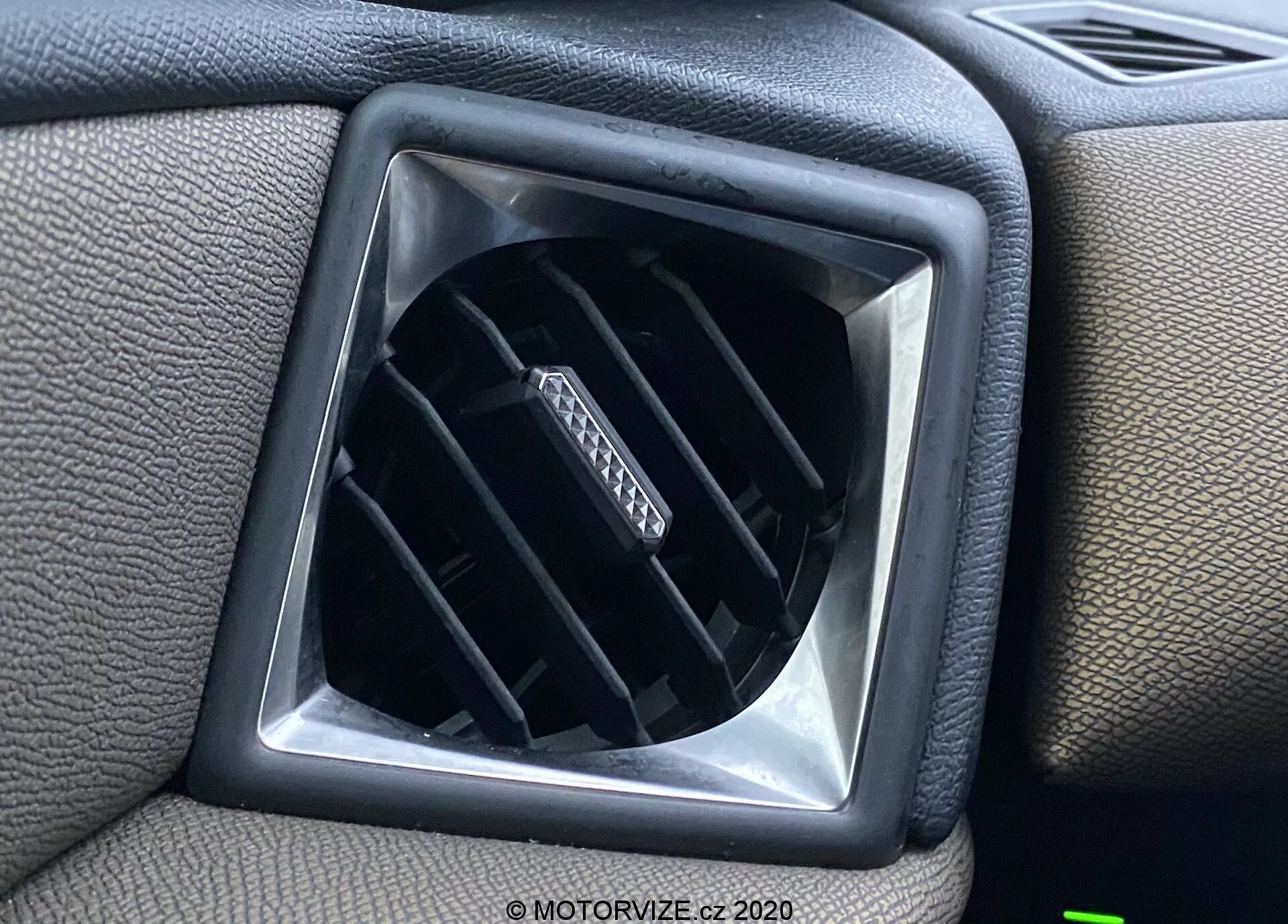 Vista ravvicinata della bocchetta d'aria nell'interno del veicolo DS Automobiles DS-3 Crossback 2019, che mostra le lamelle orizzontali regolabili all'interno di un'apertura a forma di diamante, circondata da una superficie del cruscotto in plastica testurizzata con una cornice squadrata per un ulteriore elemento di design.