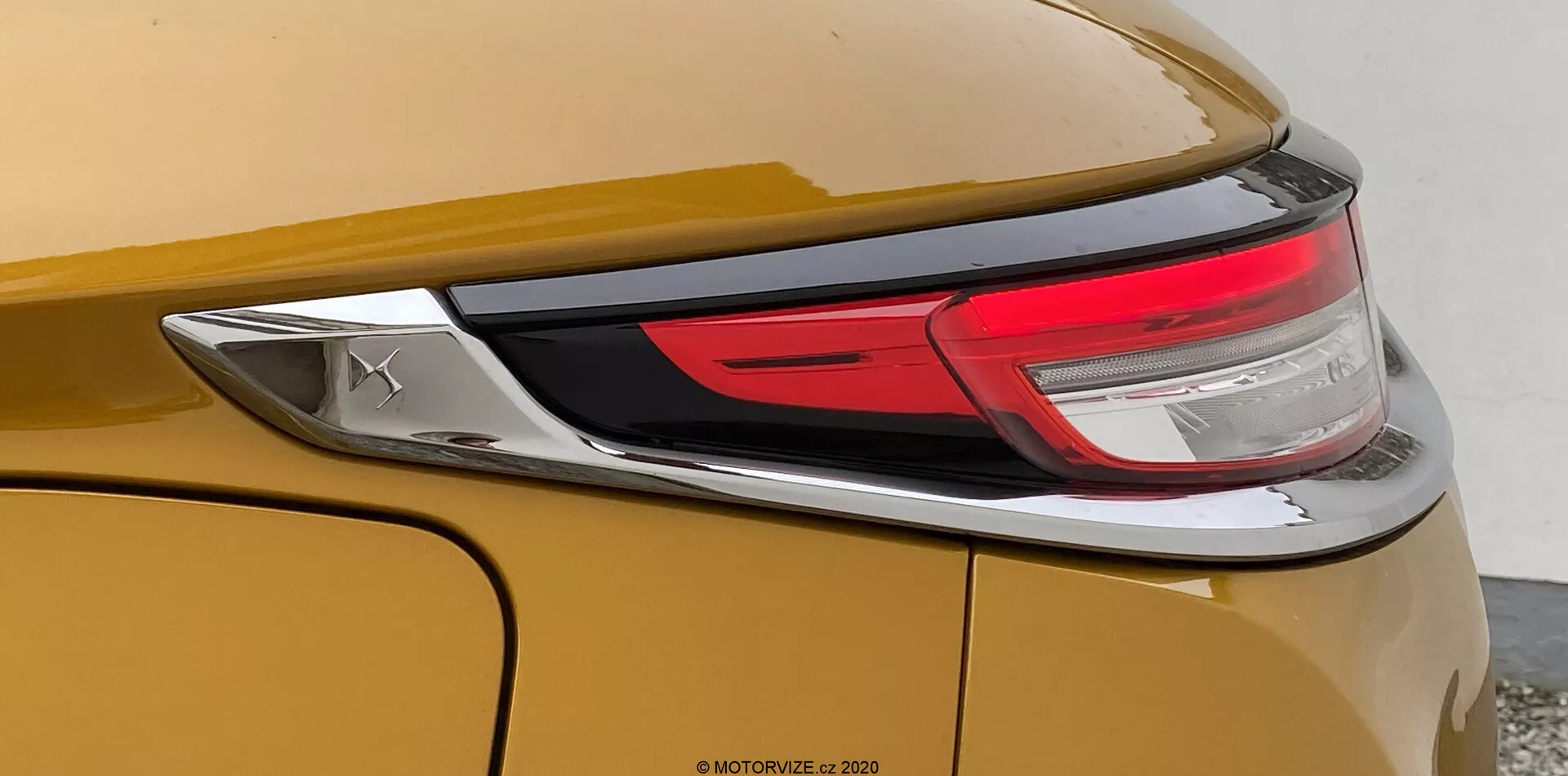 Vista ravvicinata della sezione posteriore della DS Automobiles DS-3 2019 (DS-3 Crossback). L'immagine si concentra sul lato destro del veicolo, mostrando una carrozzeria in metallo dorato o bronzo, parte del gruppo di luci posteriori LED e un pannello posteriore liscio e curvo con una linea caratteristica prominente. È visibile anche un emblema cromato, ma non identifica il marchio.