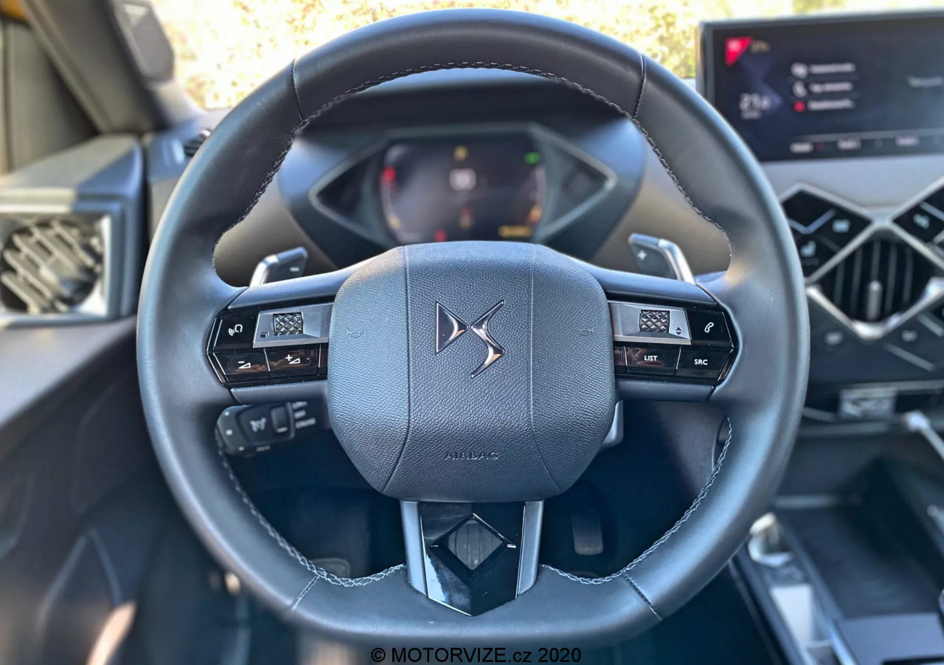 Scatto dell'interno della DS Automobiles DS-3 Crossback 2019 incentrato sul volante in pelle di lusso visto dal posto di guida. Il volante multifunzionale dispone di pulsanti di controllo per l'audio e il display delle informazioni del veicolo. Sono parzialmente visibili anche il quadro strumenti digitale e un moderno sistema di infotainment touchscreen, evidenziando le avanzate interfacce elettroniche di questo interno auto contemporaneo.