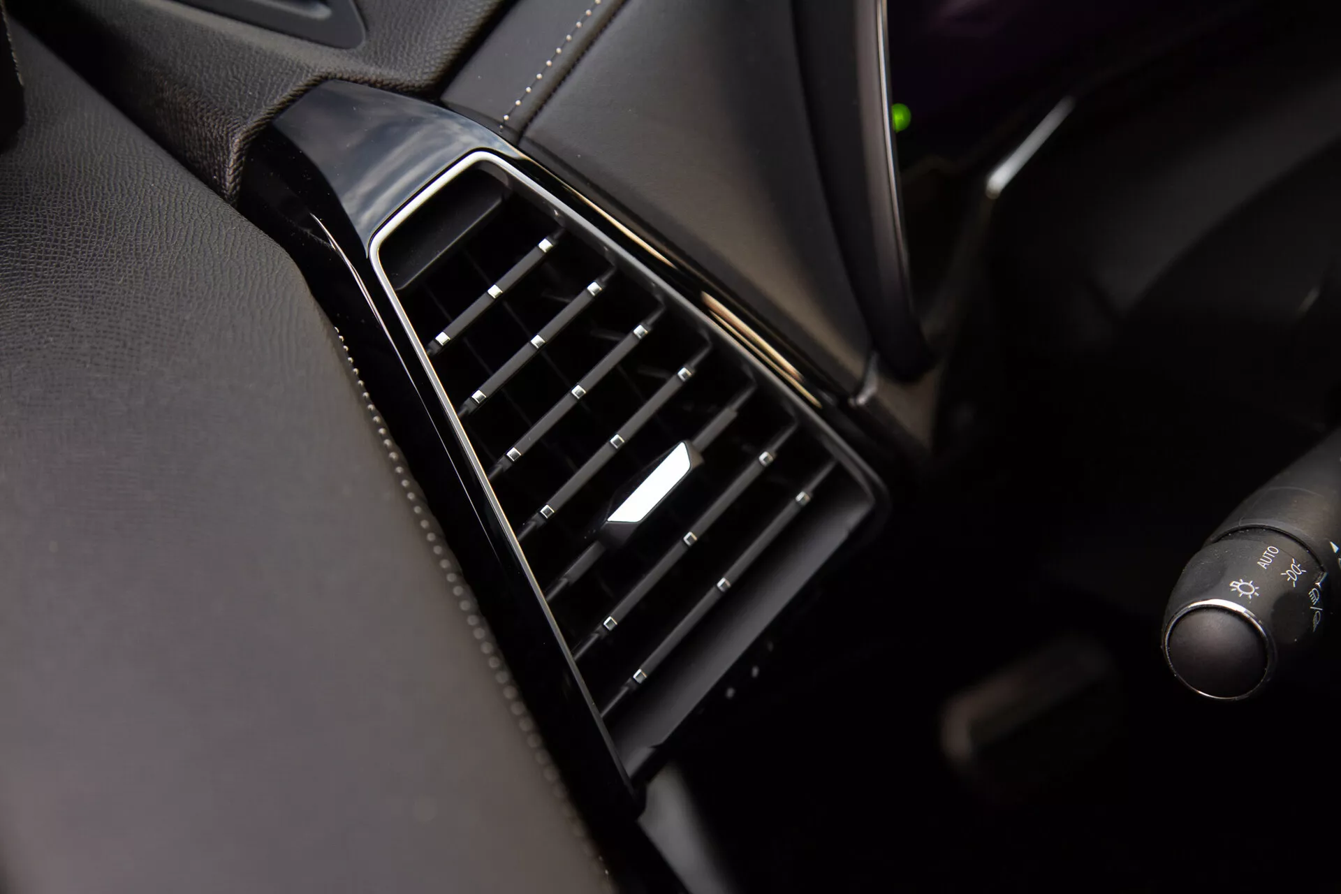 Vista ravvicinata della bocchetta d'aria della DS Automobiles DS-7 2022 sul cruscotto con lamelle nere regolabili allineate verticalmente, lunetta lucida e un accento argento sul controllo, che mostra la qualità del design interno e dei materiali del veicolo