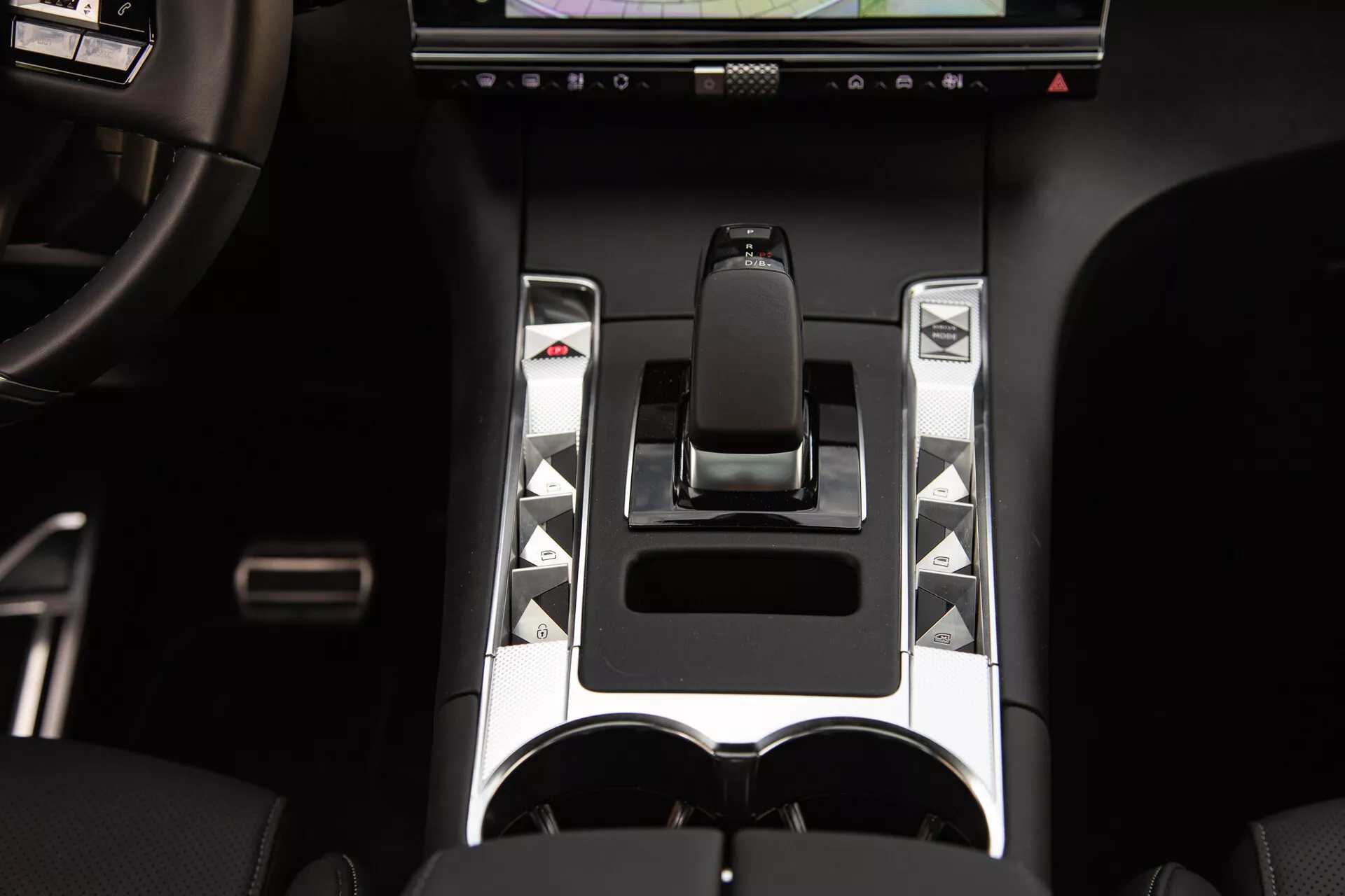 Vista dettagliata della console centrale di DS Automobiles DS-7 2022 con leva del cambio ergonomica, accenti metallici, pulsanti di controllo unici, display touch screen e doppio portabicchieri, evidenziando elementi avanzati di controllo del veicolo e di design di lusso.