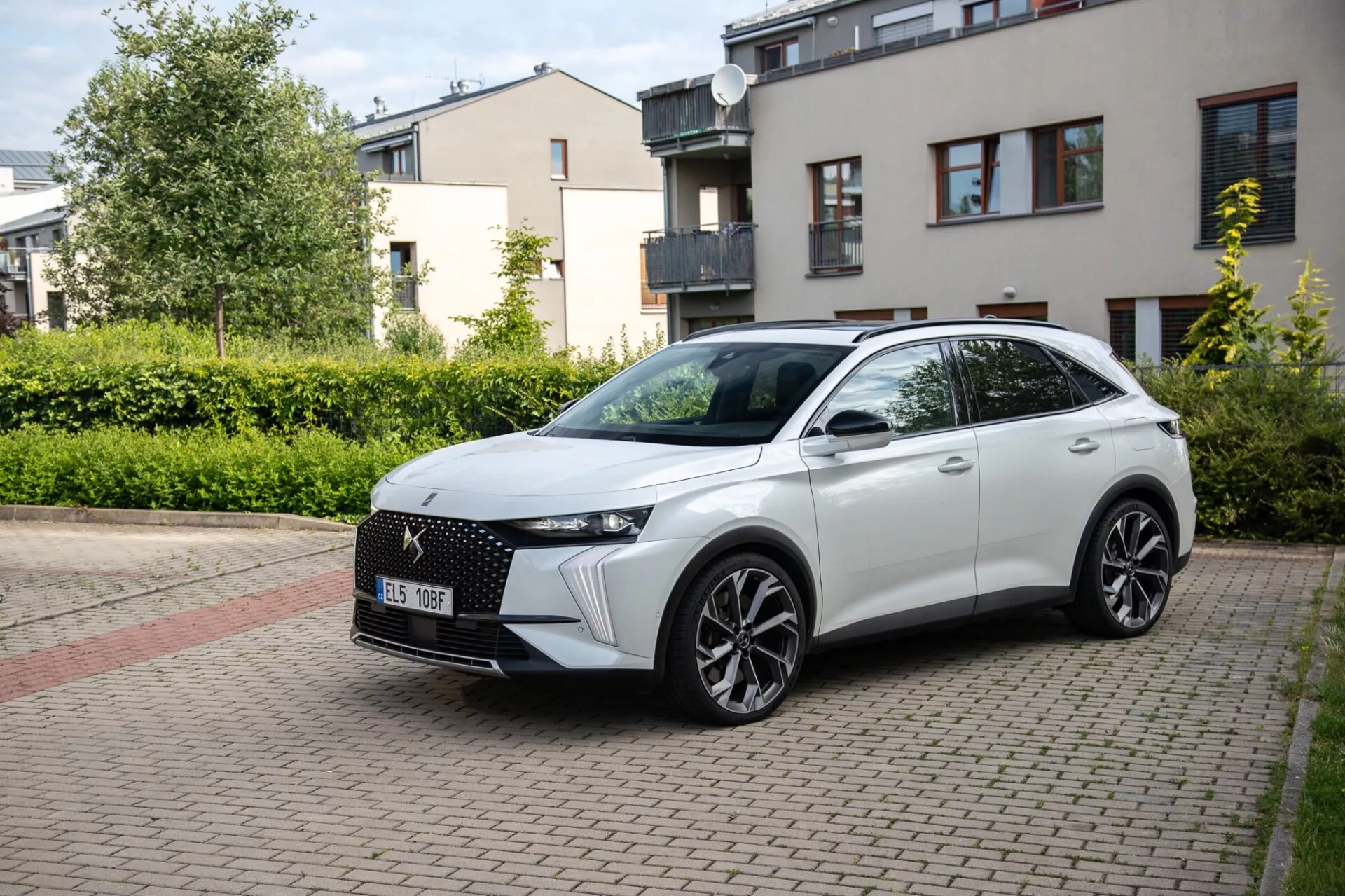 Vista frontale a tre quarti del crossover DS Automobiles DS-7 2022 parcheggiato su una strada residenziale lastricata in mattoni, che mostra il suo design moderno inclusa una griglia frontale distintiva, fari LED eleganti, cofano scolpito, grandi ruote in lega e un profilo laterale sportivo con indicatori di direzione integrati sugli specchietti laterali montati sulla porta sotto la luce naturale del giorno.