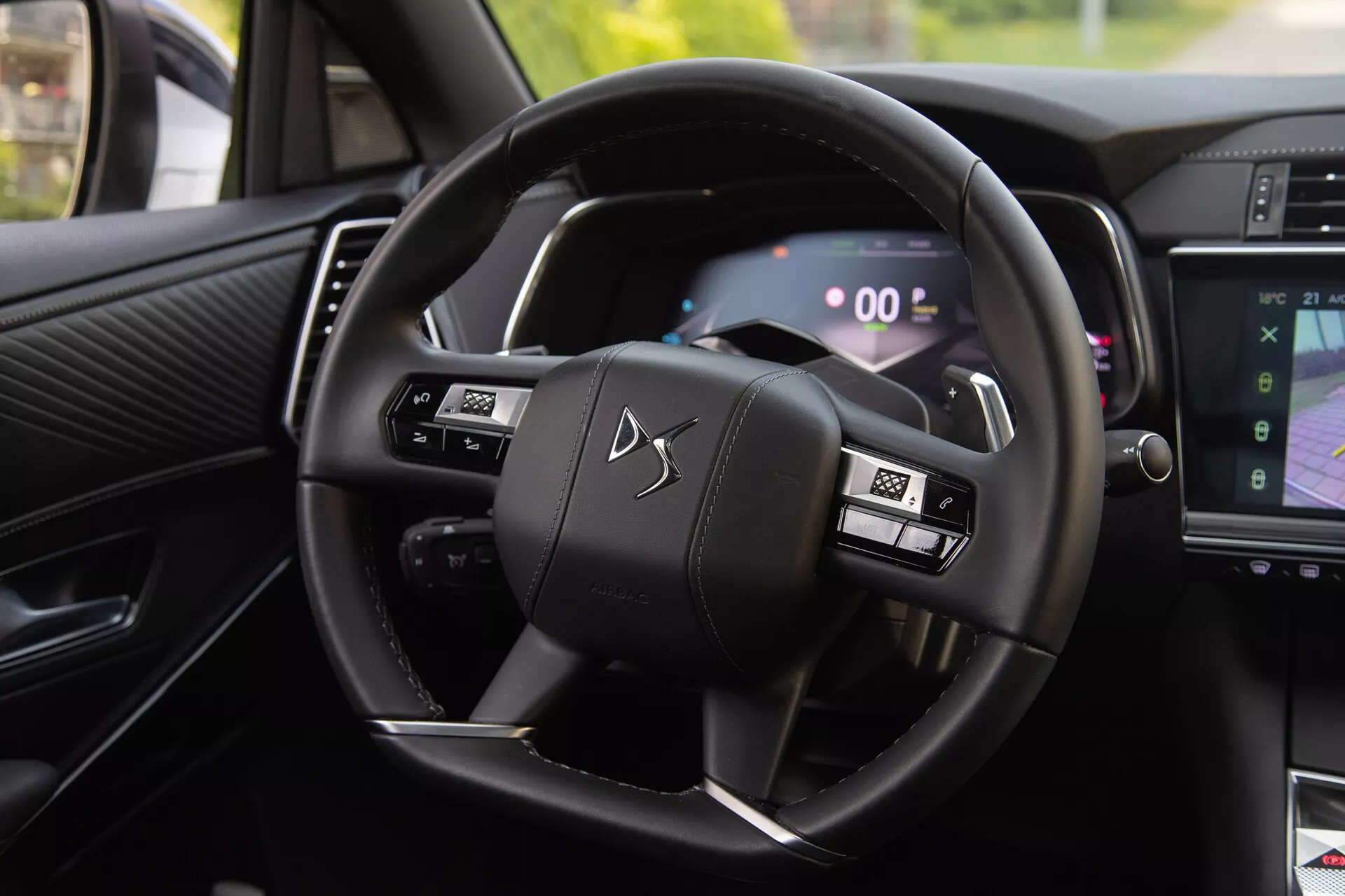Vista interna della DS Automobiles DS-7 2022 che mostra il volante con pulsanti multifunzione e il cruscotto digitale, inclusi i paddle di cambio e parte del sistema di infotainment che mostra la navigazione