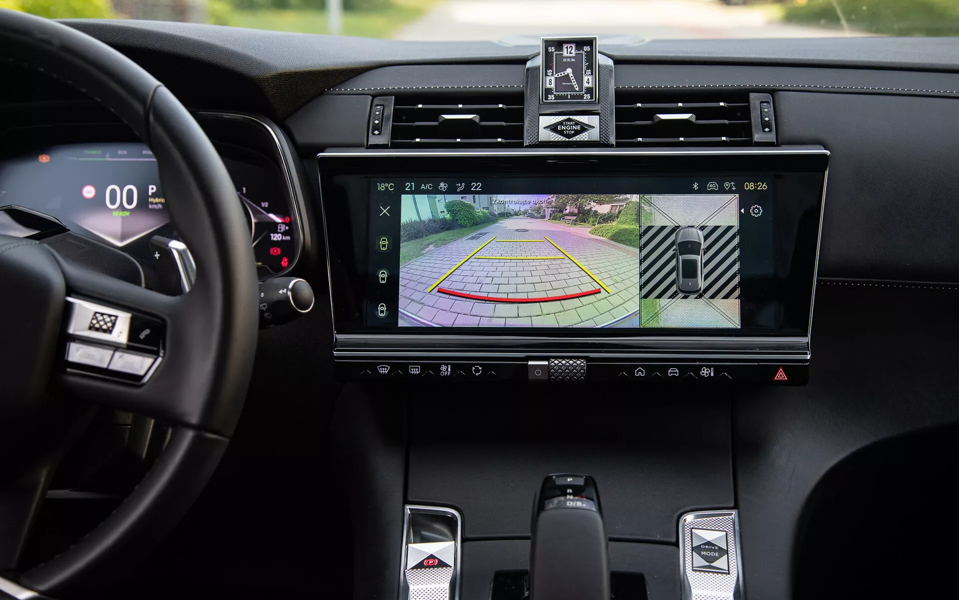 Dettaglio dell'interno lussuoso della DS-7 2022 che mostra sistema di infotainment con display della telecamera posteriore e linee guida dinamiche per l'assistenza al parcheggio, bocchette d'aria centrali, pulsanti di controllo del clima, leva del cambio sportiva e tachimetro digitale