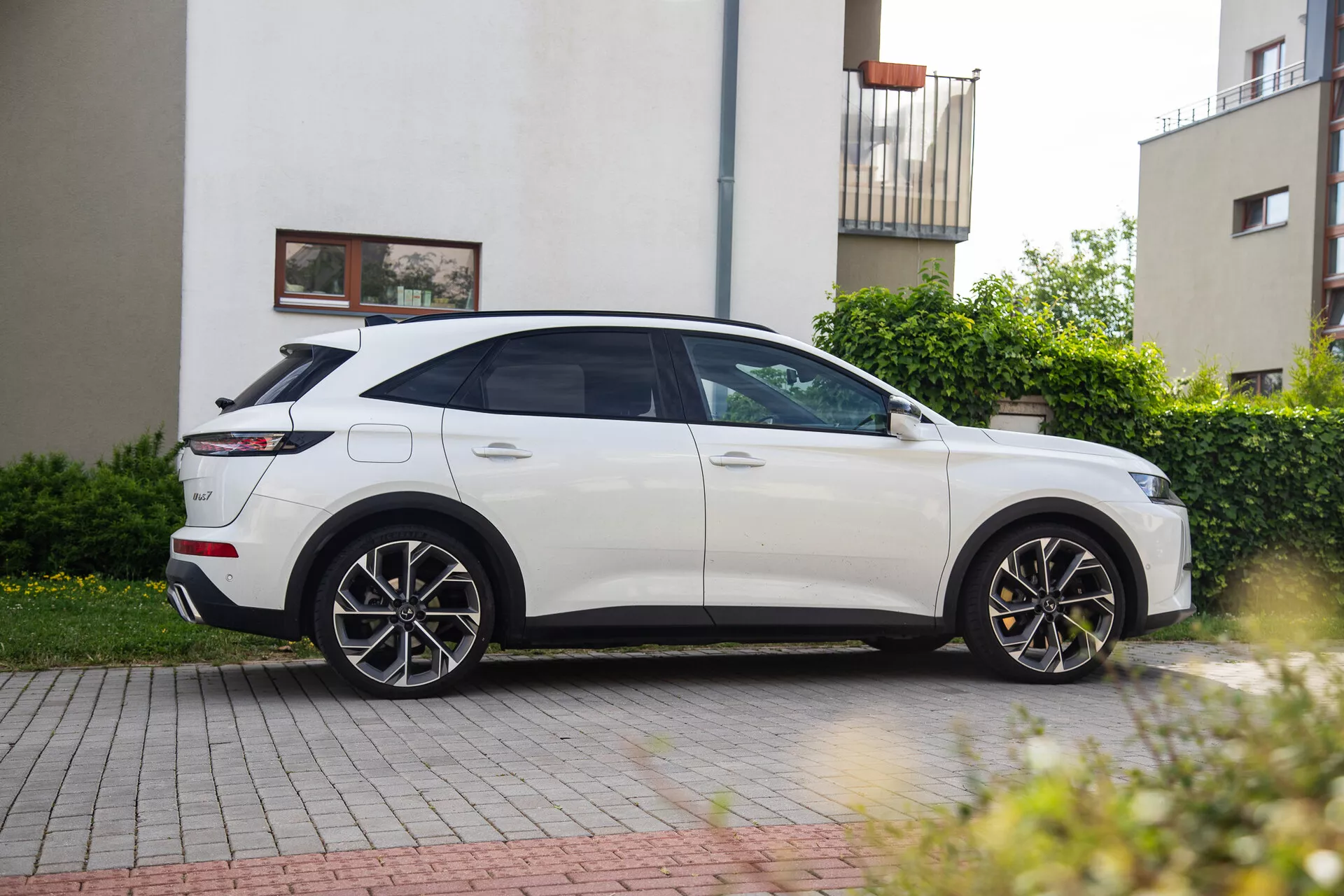 Profilo laterale del SUV bianco DS Automobiles DS-7 2022 parcheggiato in via residenziale che mostra design elegante, linee aerodinamiche, grandi ruote in lega, fari LED, specchietti laterali e tetto panoramico