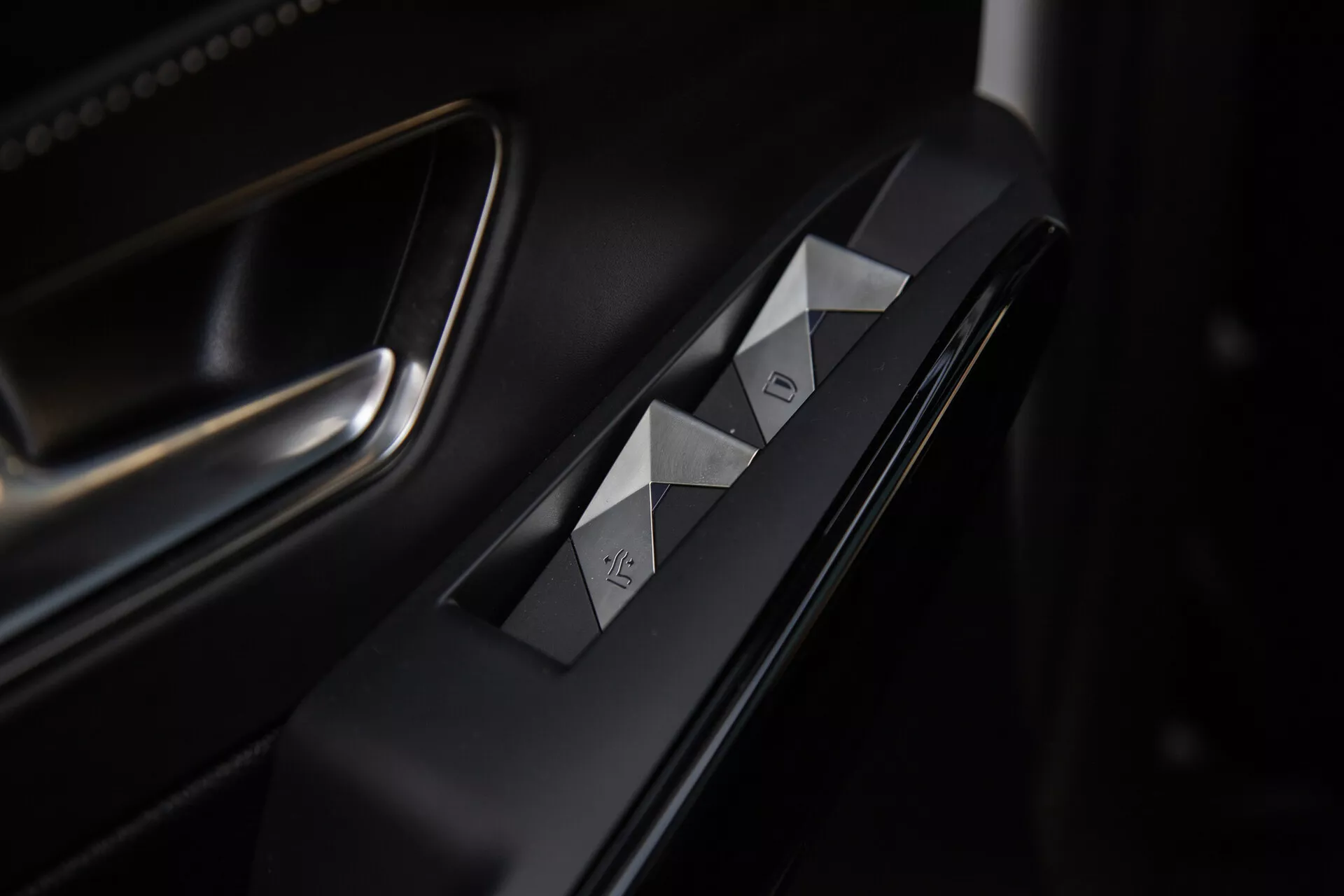Visuale dettagliata dei comandi sulla porta lato guidatore della DS Automobiles DS-7 2022 con interruttori per i vetri a taglio di diamante, pulsante di bloccaggio della porta, finiture premium in matte e metallo e illuminazione sofisticata che mette in risalto il design ergonomico.