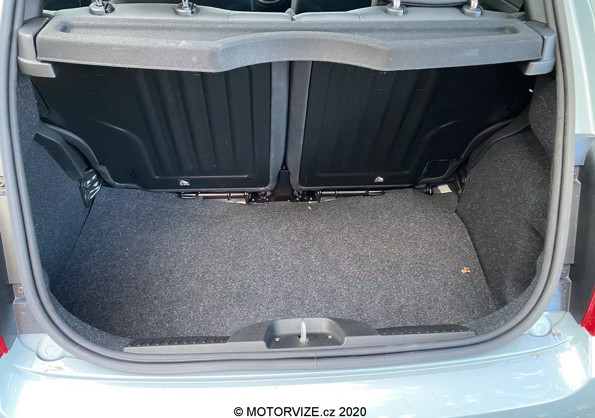 Vista ravvicinata del bagagliaio della Fiat 500 del 2015 da un punto di vista posteriore con il coperchio aperto, che mostra un'area di carico rivestita in moquette e piatta con scomparti laterali in plastica e una maniglia sul pavimento del bagagliaio. L'immagine evidenzia la spaziosità, l'utilizzabilità e le condizioni pulite e ben illuminate del bagagliaio.