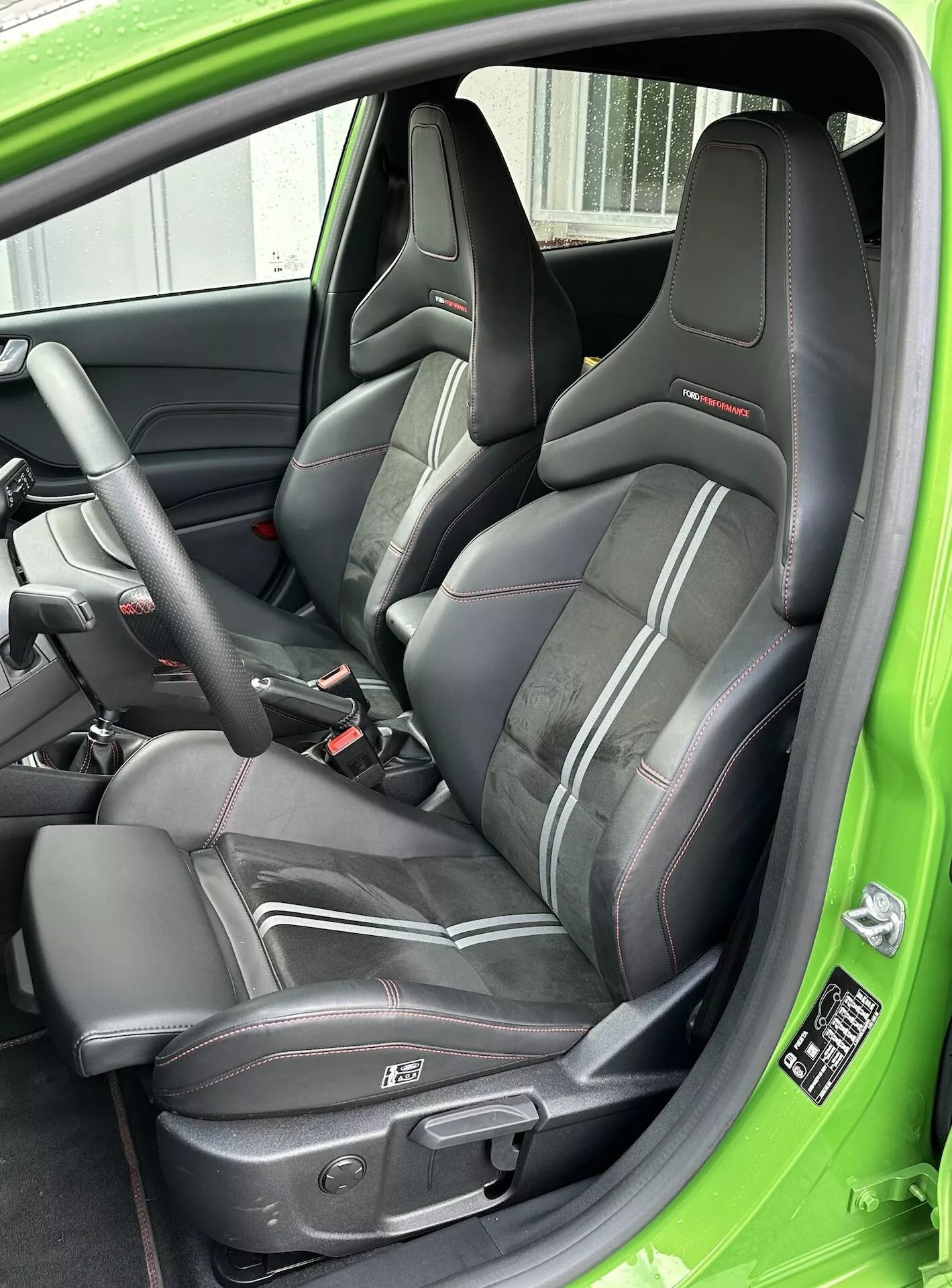 Vista ravvicinata del sedile sportivo del conducente in pelle con bordino rosso, cintura di sicurezza a tre punti e comandi elettrici del sedile, accentuato da un rivestimento interno verde della Ford Fiesta 2022.