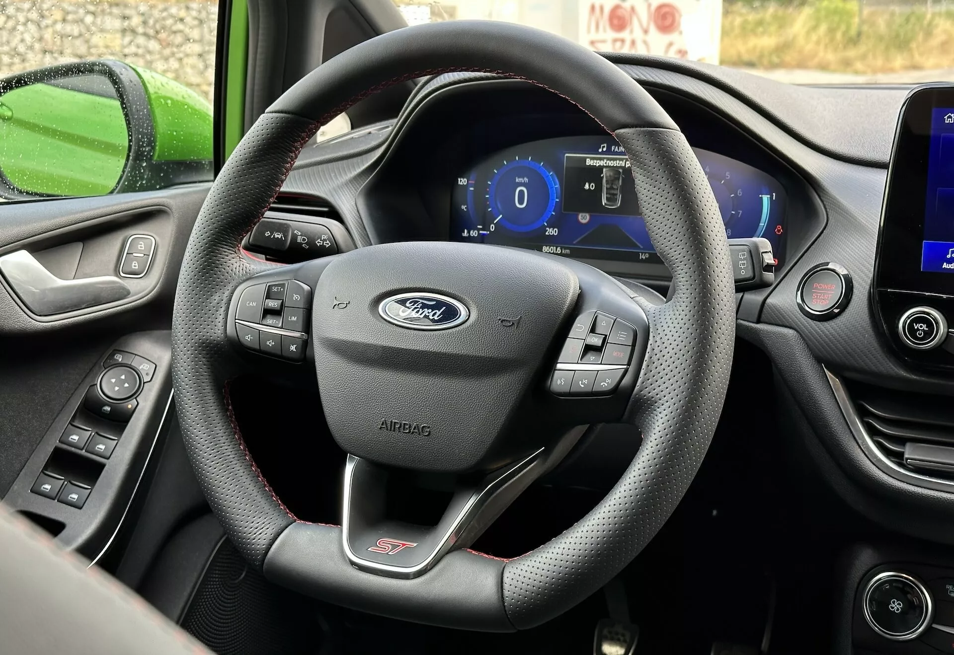 Vista interna della Ford Fiesta 2022 focalizzata sul volante a tre razze rivestito in pelle con comandi multifunzione e cruscotto digitale dalla prospettiva del sedile del guidatore