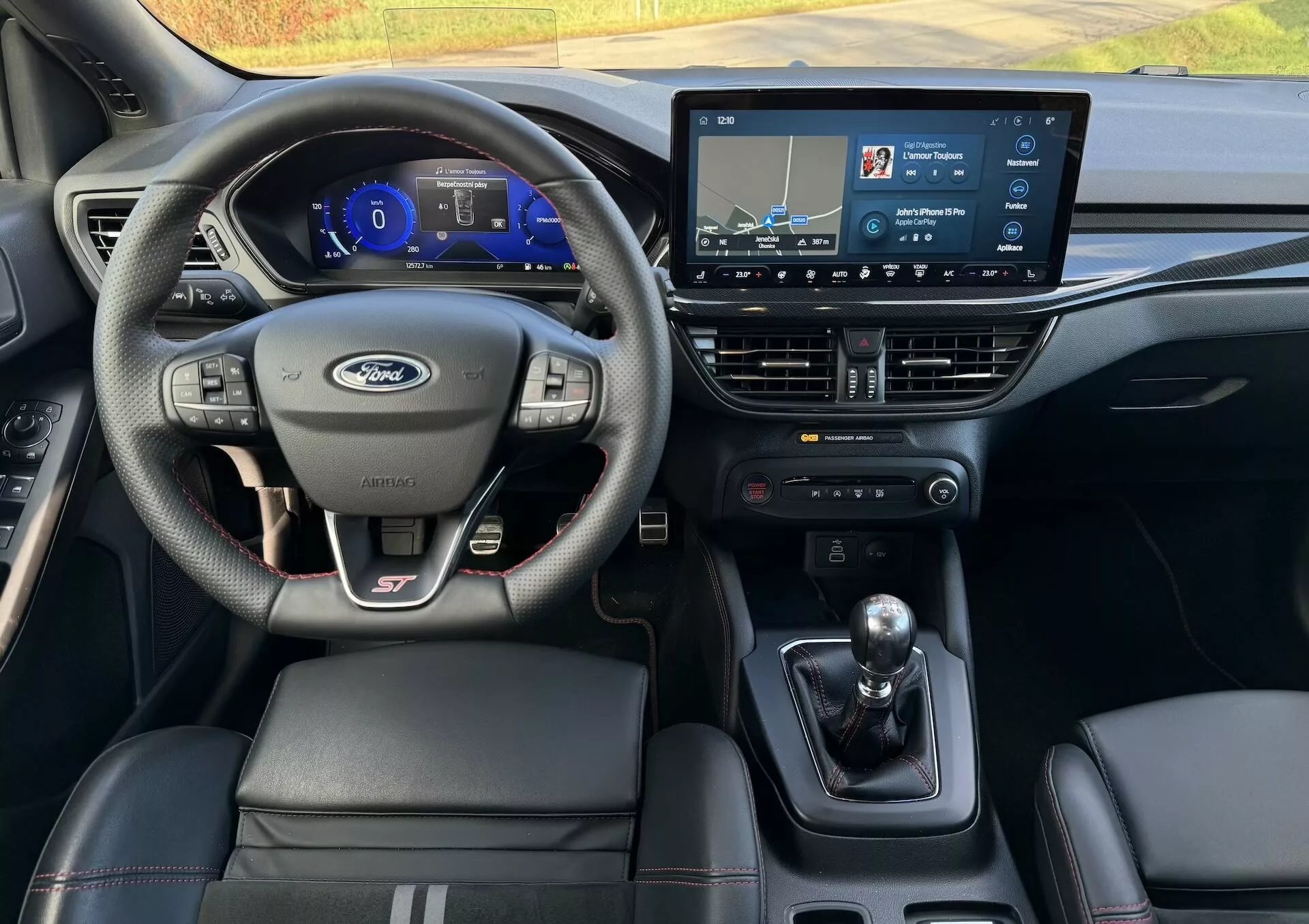 Interni della Ford Focus ST 2022 dal punto di vista del conducente che mettono in evidenza il volante multifunzione rivestito in pelle con branding ST, cruscotto digitale, sistema di infotainment touch screen, trasmissione manuale e sedili in pelle.