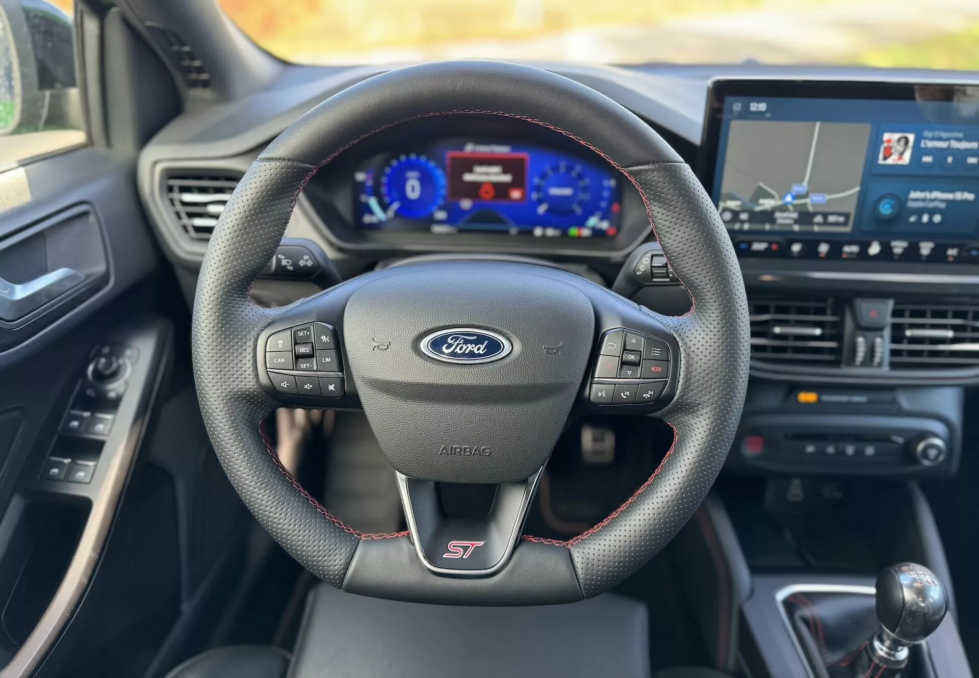 Vista interna del Ford Focus ST 2022 che mette in evidenza il volante sportivo multifunzione con logo del produttore e designazione del modello, cruscotto digitale e sistema di infotainment touchscreen con navigazione