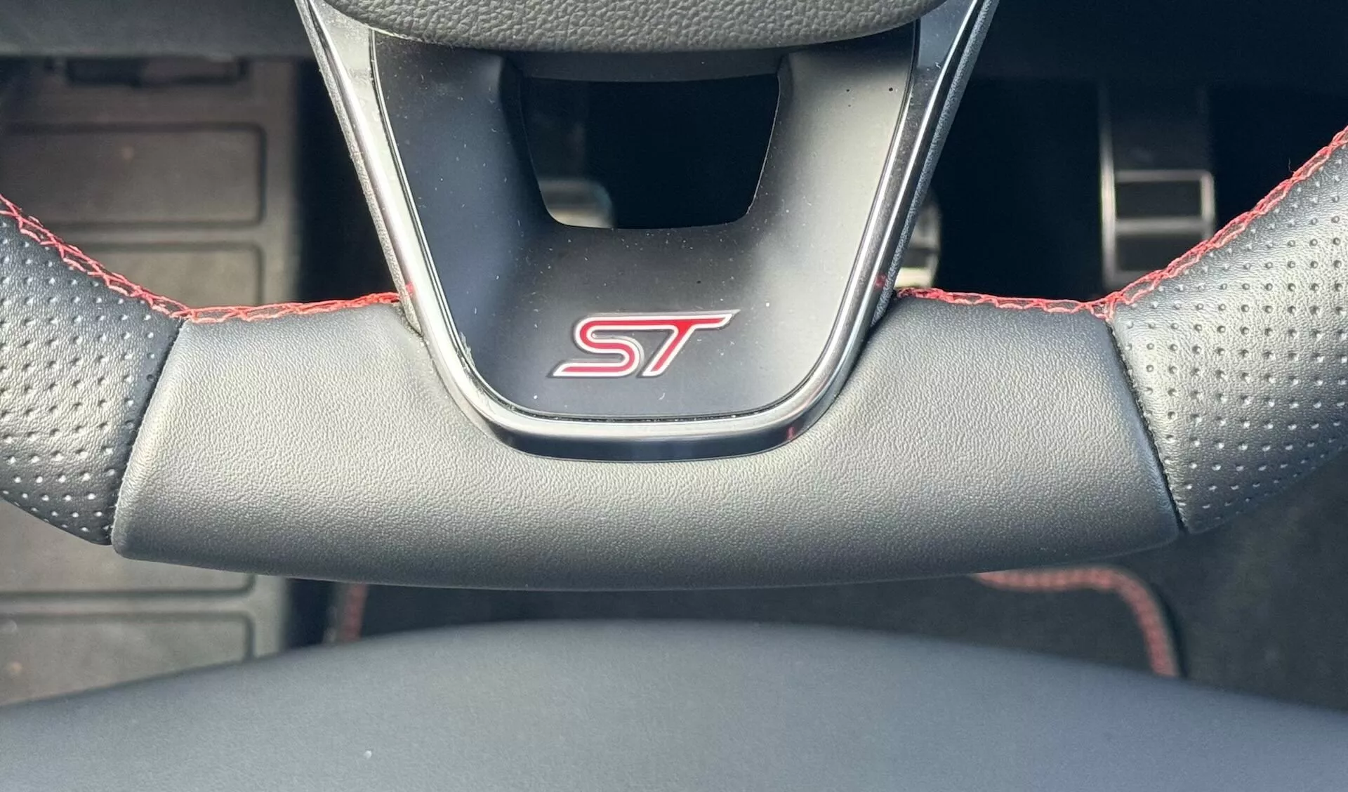 Primo piano del volante della Ford Focus ST 2022 con distintivo ST, impugnatura in pelle perforata con cuciture rosse, dalla prospettiva del conducente