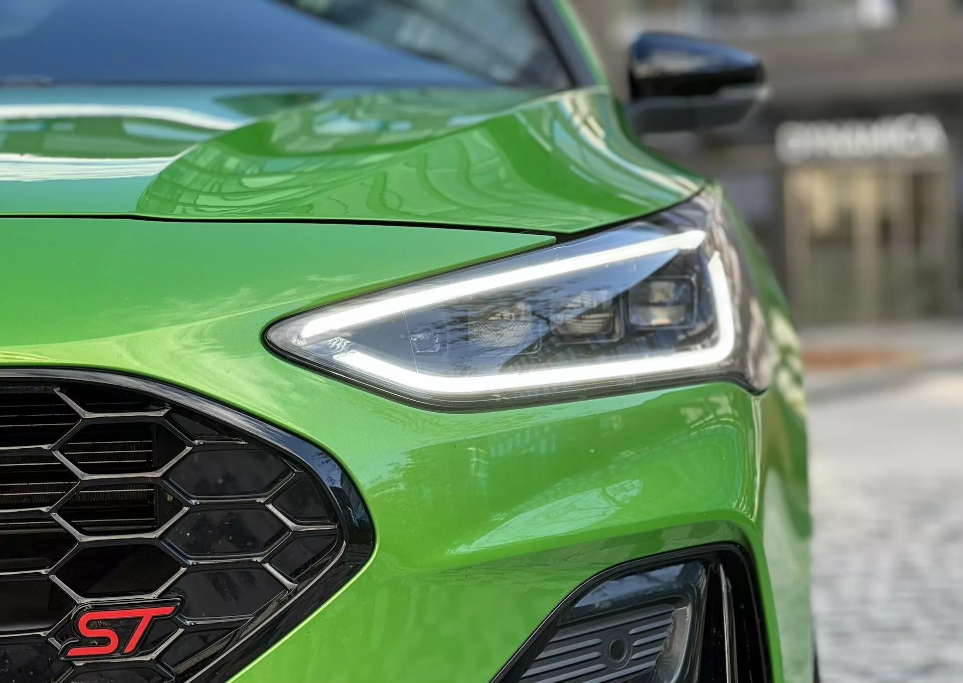 Primo piano del quarto anteriore sinistro della Ford Focus ST 2022 con fari LED, griglia a nido d'ape e cofano scolpito in verde brillante