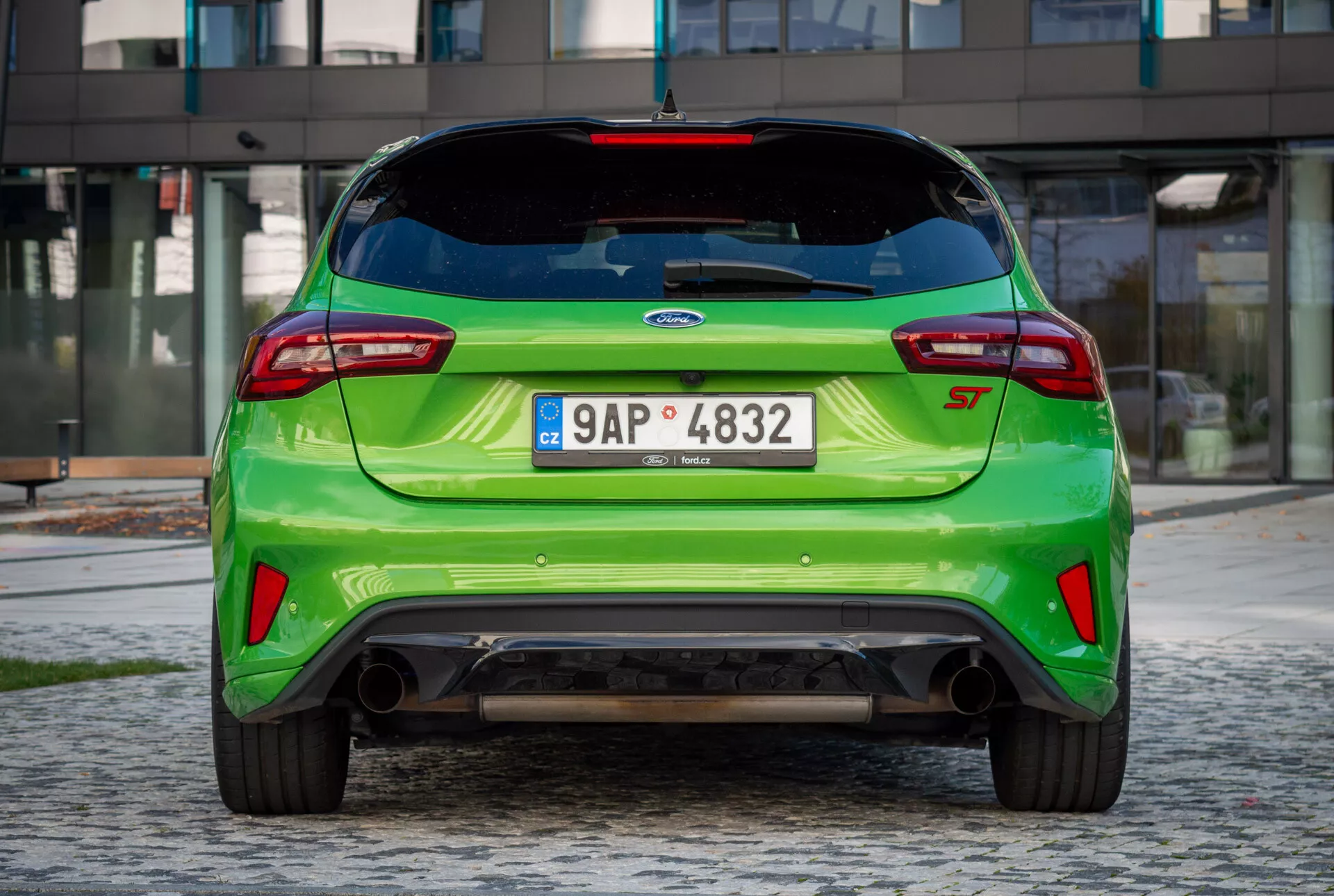 Vista posteriore di Ford Fiesta ST 2022 verde brillante con spoiler sul tetto, badge EcoBoost, doppie uscite di scarico e diffusore posteriore su sfondo di ciottoli