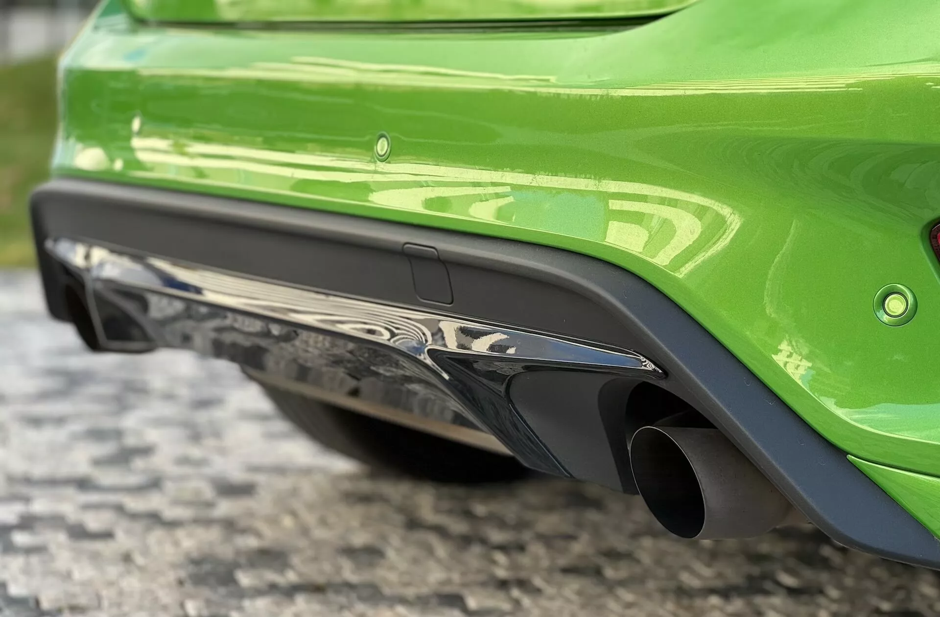 Vivace Ford Focus ST verde 2022 che mostra il suo paraurti posteriore lucido con doppio scarico cromato e diffusore aerodinamico da un'angolazione bassa su una superficie di ciottoli.