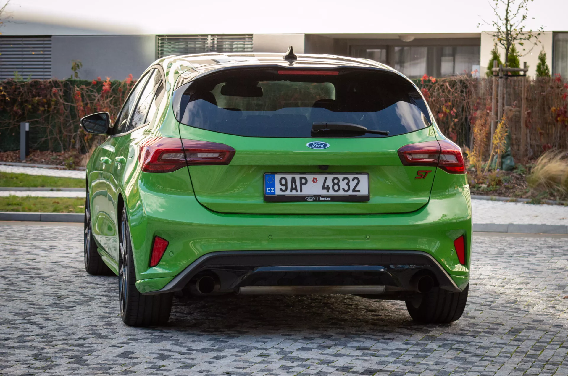 Prospettiva posteriore di Ford Focus ST 2022 in verde brillante su ciottoli, con spoiler, doppio scarico e emblema del produttore