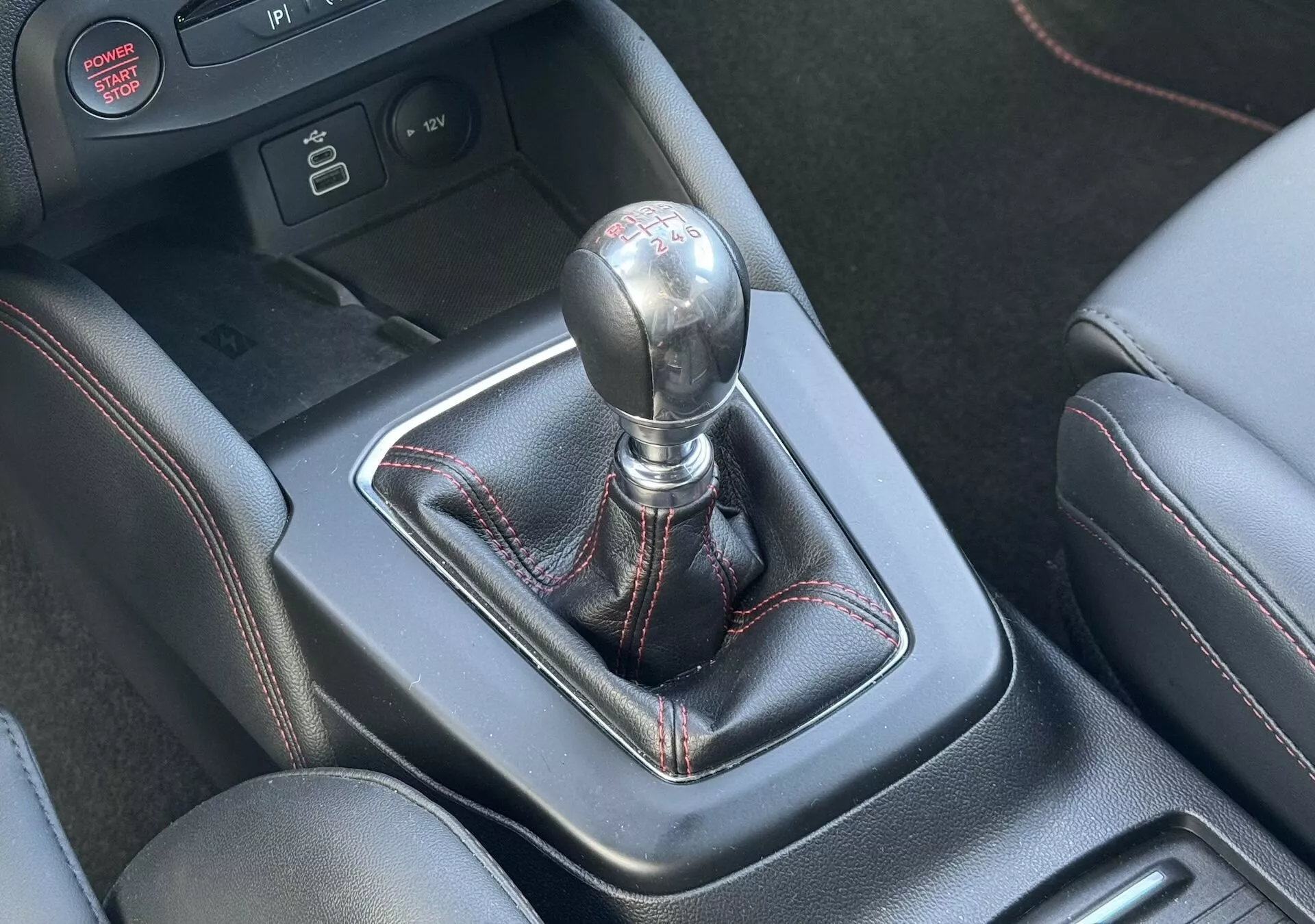 Primo piano del cambio manuale della Ford Focus ST 2022 con pomello metallico, cuffia in pelle con cuciture rosse e console centrale con assistenti di guida all'avanguardia