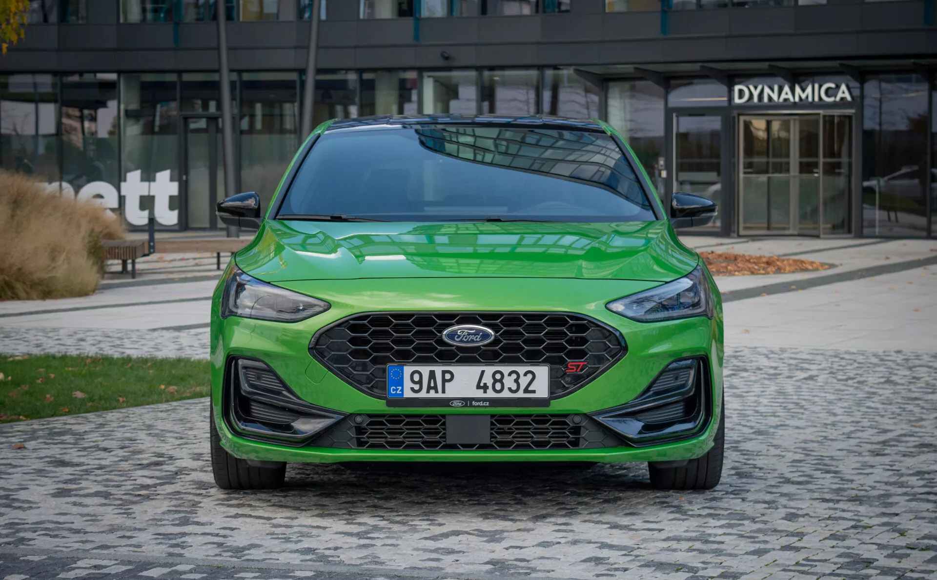 Vista frontale della berlina Ford Focus ST 2022 verde che mostra la griglia esagonale con design cromato e a nido d'ape, emblema Ford al centro, paraurti aerodinamico con fari antinebbia integrati, fari LED con luci di marcia diurna, e montanti del parabrezza robusti per una maggiore sicurezza