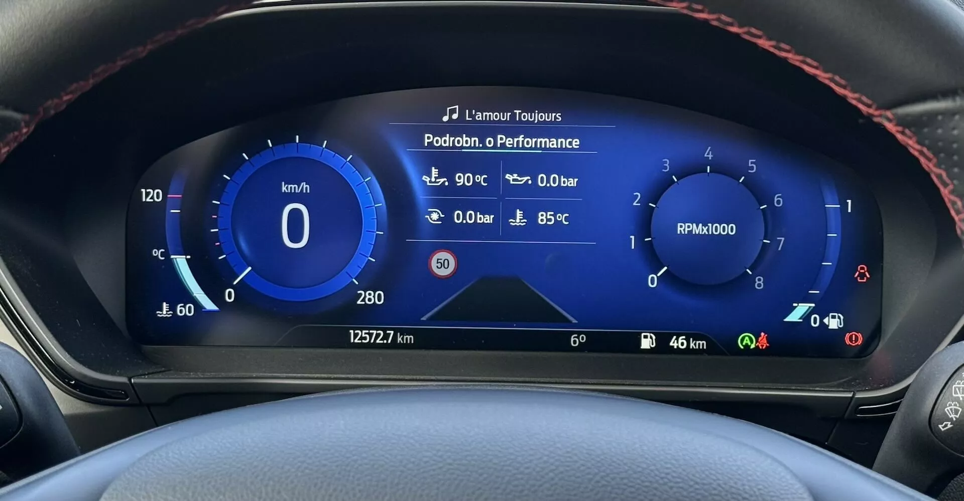 Vista ravvicinata del cruscotto digitale della Ford Focus ST 2022 che mostra tachimetro, contagiri, temperatura esterna, pressione del turbo e temperatura del refrigerante con cuciture rosse sportive sul bordo del volante