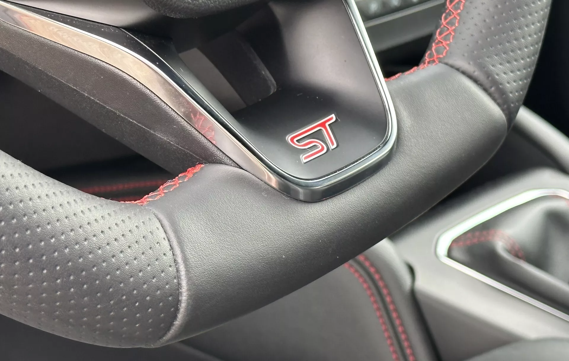 Vista ravvicinata del volante della Ford Focus 2022 con design sportivo, pelle forata, cuciture a contrasto rosse e logo 'ST', indicativo di un modello prestazionale