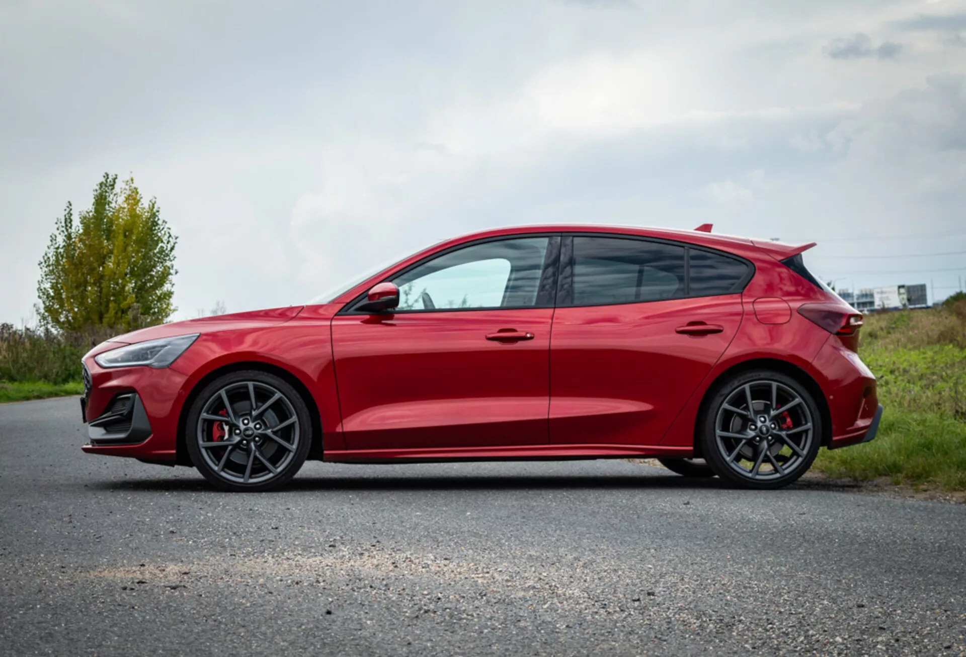 Ford Focus hatchback rosso 2022 che mostra le caratteristiche di design dal profilo laterale con ruote in lega, aerodinamica sportiva e parcheggiato su una strada asfaltata contro uno sfondo di paesaggio naturale