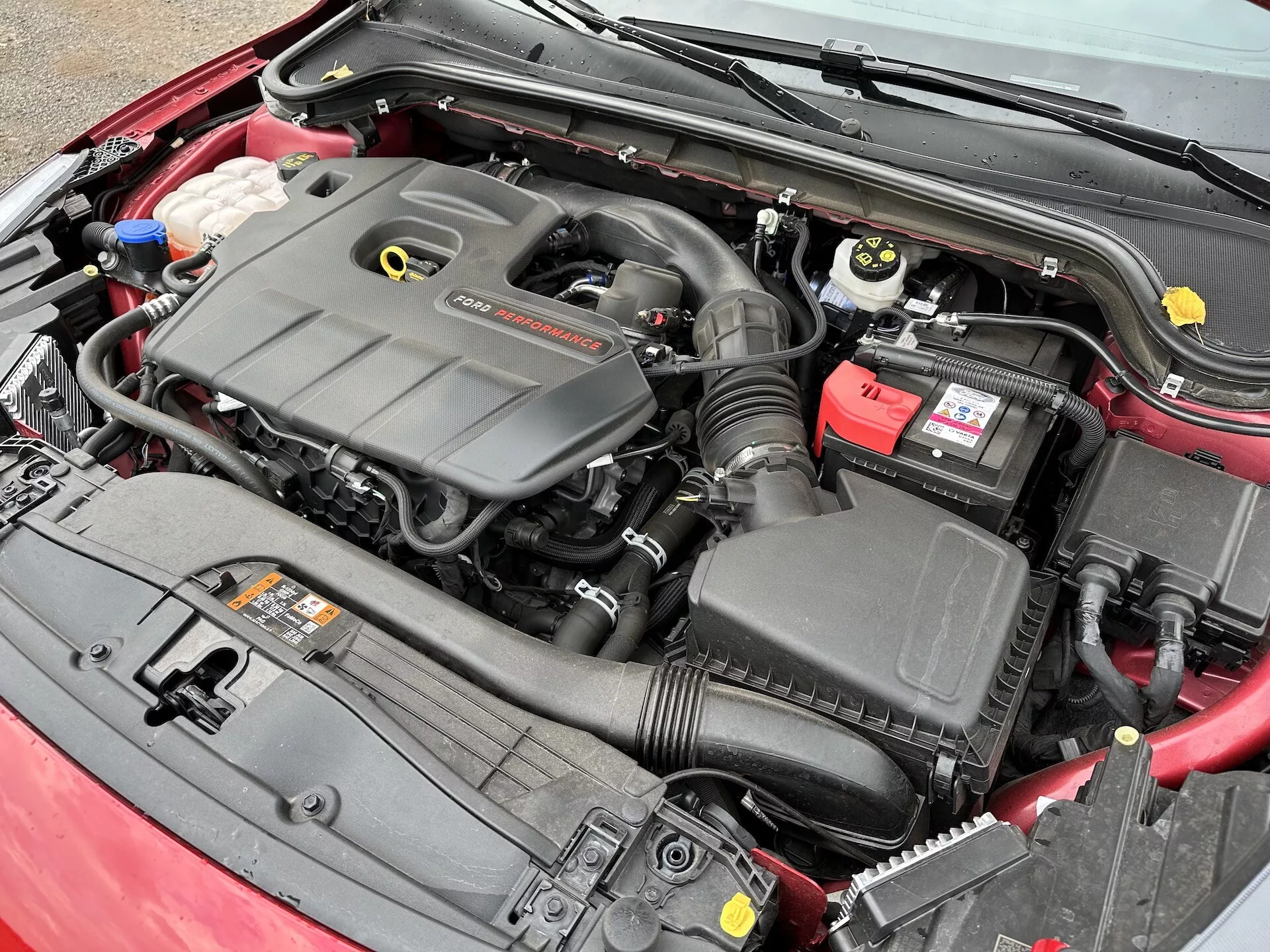 Vista ravvicinata del vano motore della Ford Focus 2022 che mostra il blocco motore, il sistema di aspirazione aria, la batteria e i serbatoi dei fluidi da un'angolazione elevata