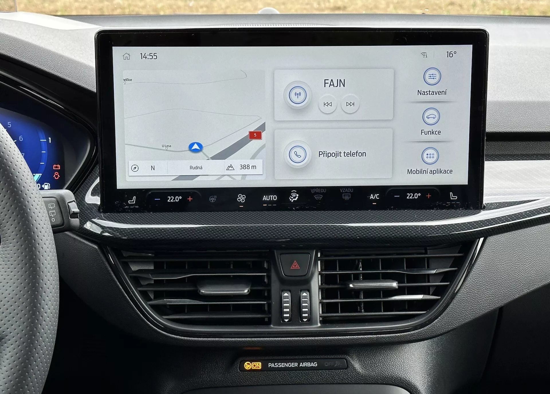 Vista della console centrale della Ford Focus 2022 dalla prospettiva del conducente, evidenziando il grande sistema di infotainment con schermo touch che visualizza la navigazione e le impostazioni in ceco, controllo della temperatura a doppia zona, e design moderno ed elegante