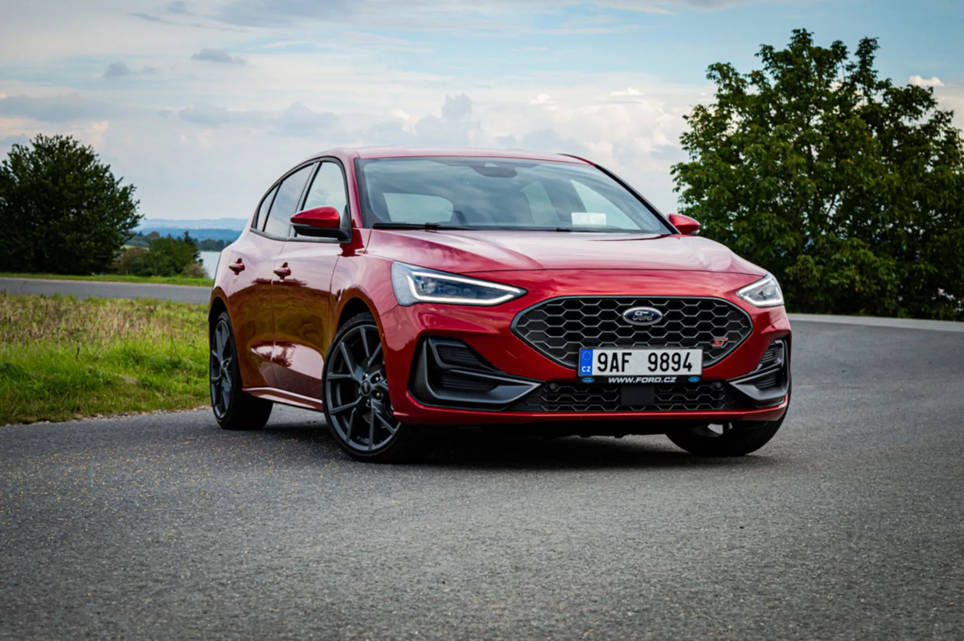 Ford Focus rosso hatchback 2022 su strada asfaltata, che mostra fari LED eleganti, ruote in lega sportive e un design moderno con linee distintive e grande griglia frontale contro un cielo nuvoloso con accenni di verdeggianti campagne
