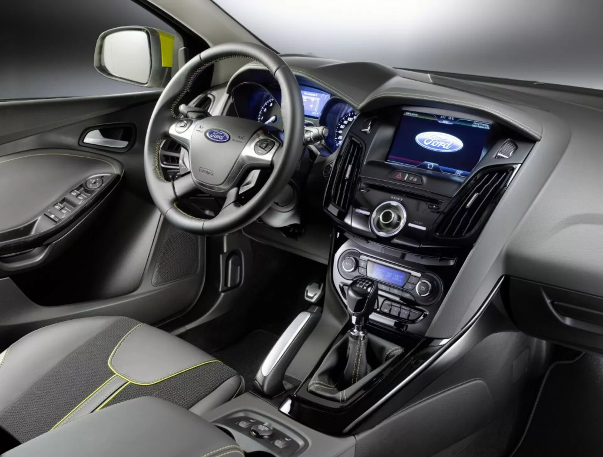 Vista interna di una Ford Focus 2011 con cruscotto, area del guidatore, volante con logo Ford, quadro strumenti illuminato, schermo touch centrale per l'infotainment, controlli del clima, sistema audio, leva del cambio automatico e sedile del passeggero anteriore con rivestimento in tessuto e motivo di cuciture