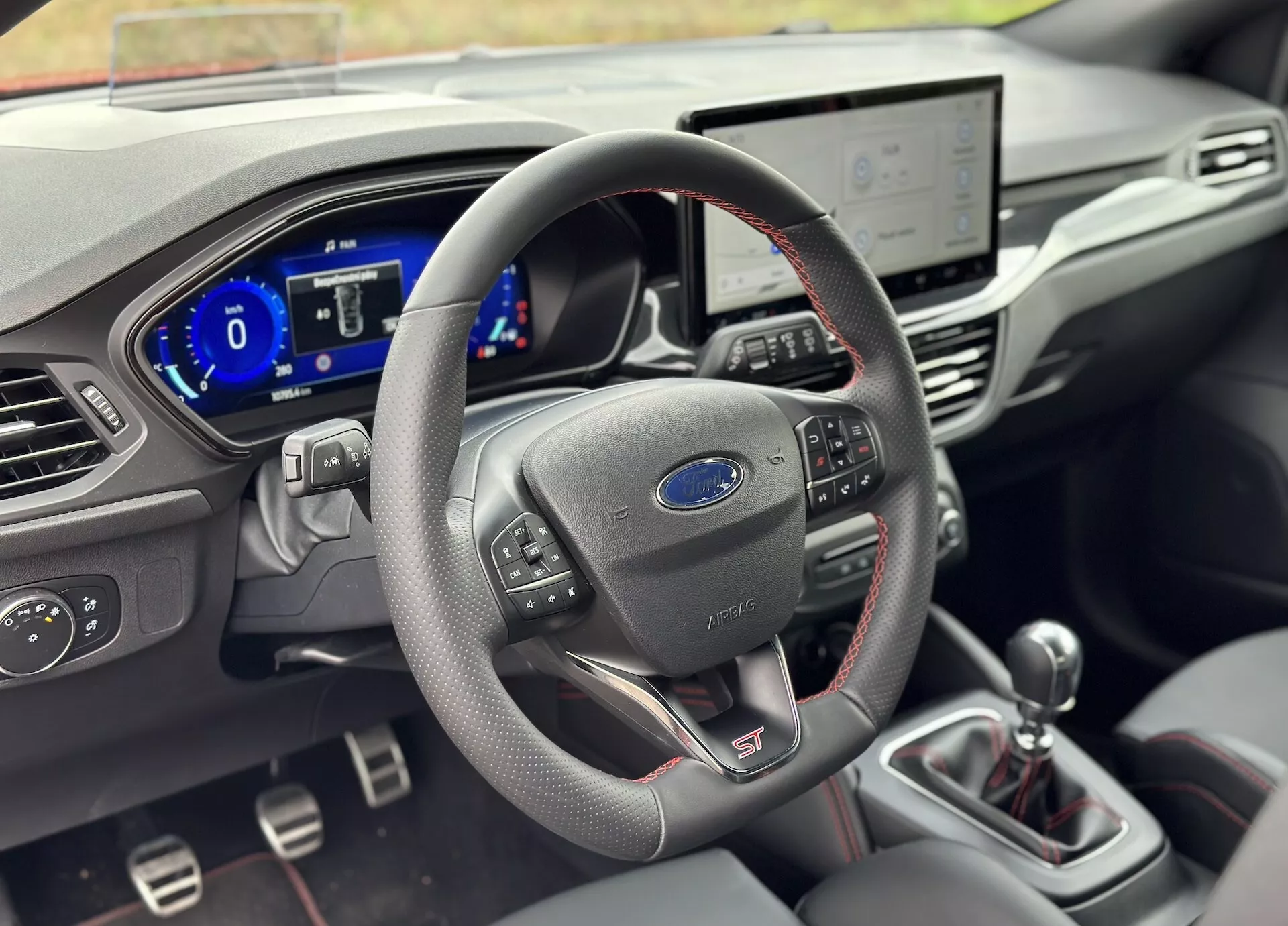 Interni Ford Focus 2022 con volante rivestito in pelle con comandi integrati e badge 'ST', cruscotto digitale, sistema di infotainment touch, comandi per il clima e leva del cambio manuale con materiali premium dettagliati e messa a fuoco con profondità di campo ridotta