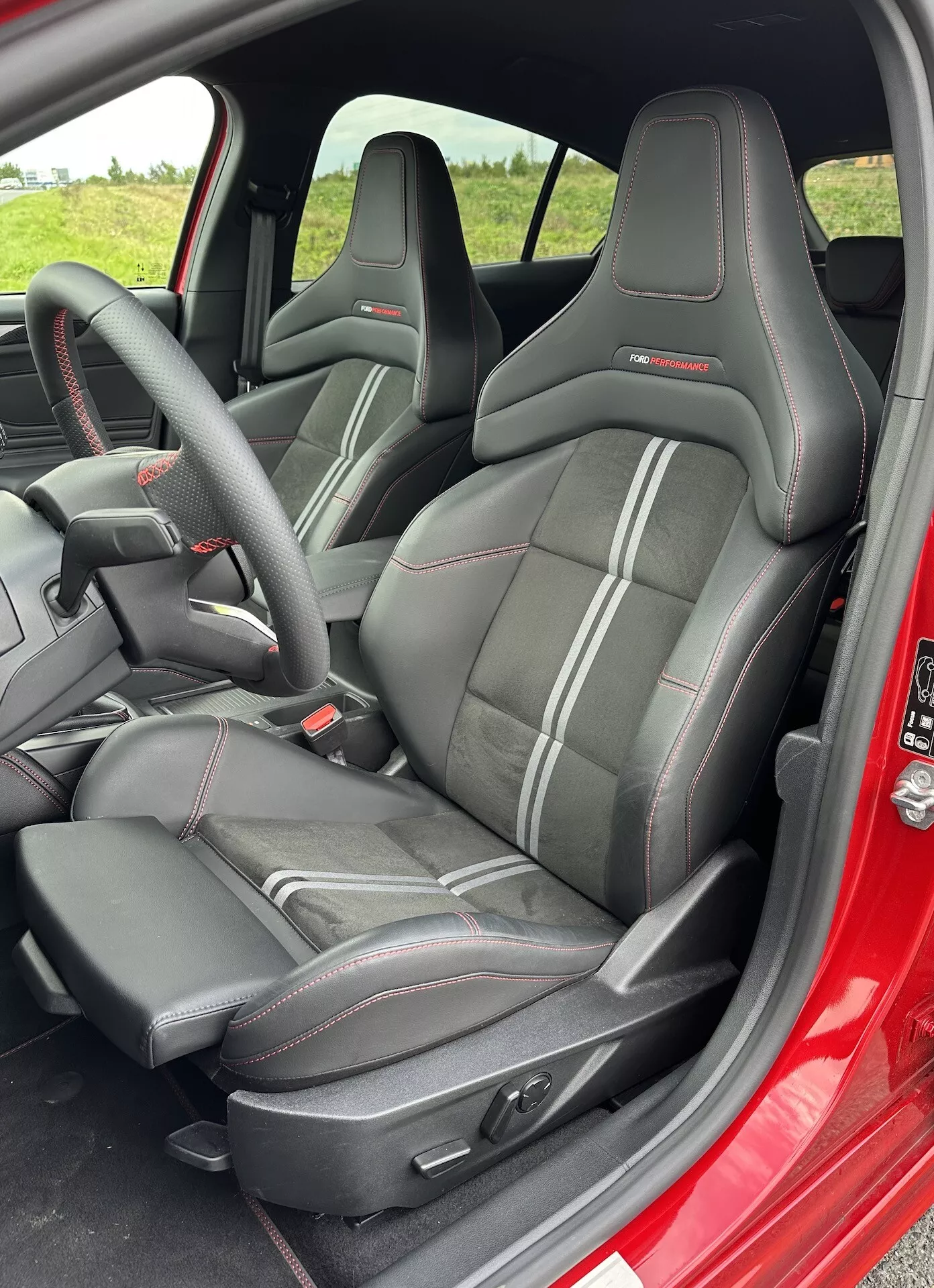 Interni Ford Focus 2022 con sedili a guscio sportivi con schienale alto e poggiatesta integrati, rivestimenti neri con cuciture a contrasto e comandi di regolazione sedile elettronici, dalla prospettiva della porta lato conducente