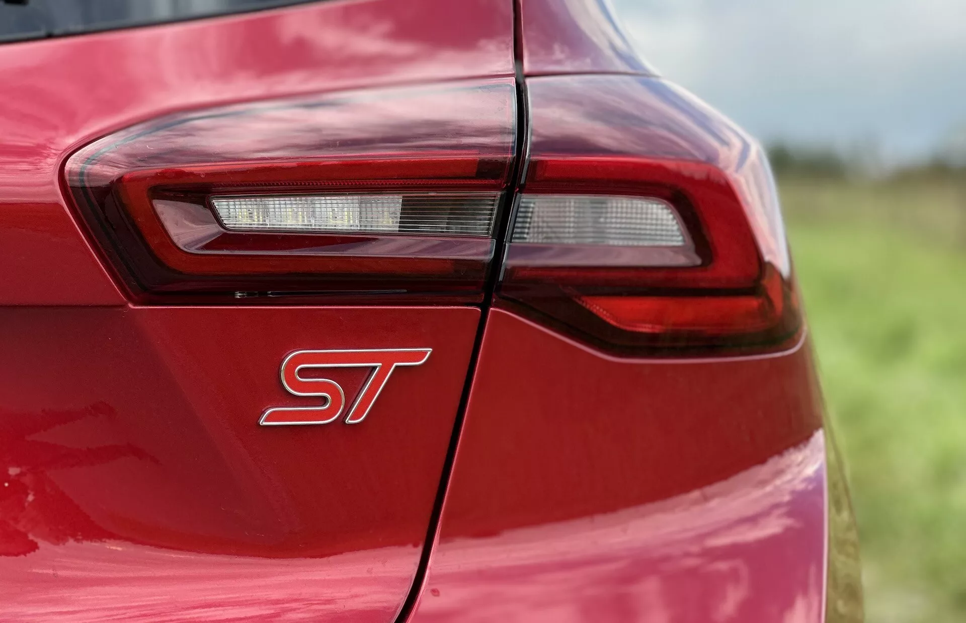 Primo piano del quarto posteriore della Ford Focus ST 2022 con carrozzeria rosso vivace, badge sportive e design del fanale posteriore LED