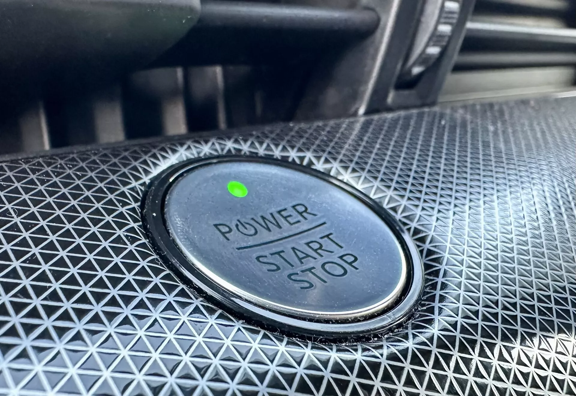Vista ravvicinata del pulsante di accensione/spegnimento in una Ford Mustang-Mach-E 2020, caratterizzato dalla scritta 'POWER START STOP', luce indicatrice verde e design texture circostante
