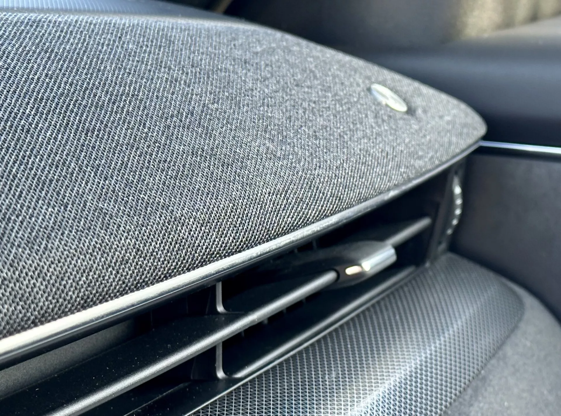 Vista ravvicinata dell'interno della Ford Mustang Mach-E 2020 che mostra una parte del cruscotto o del pannello della porta con una griglia del diffusore in tessuto premium integrata, un emblema che suggerisce una partnership con un produttore di apparecchiature audio di alta gamma, accanto a una bocchetta d'aria nera lucida